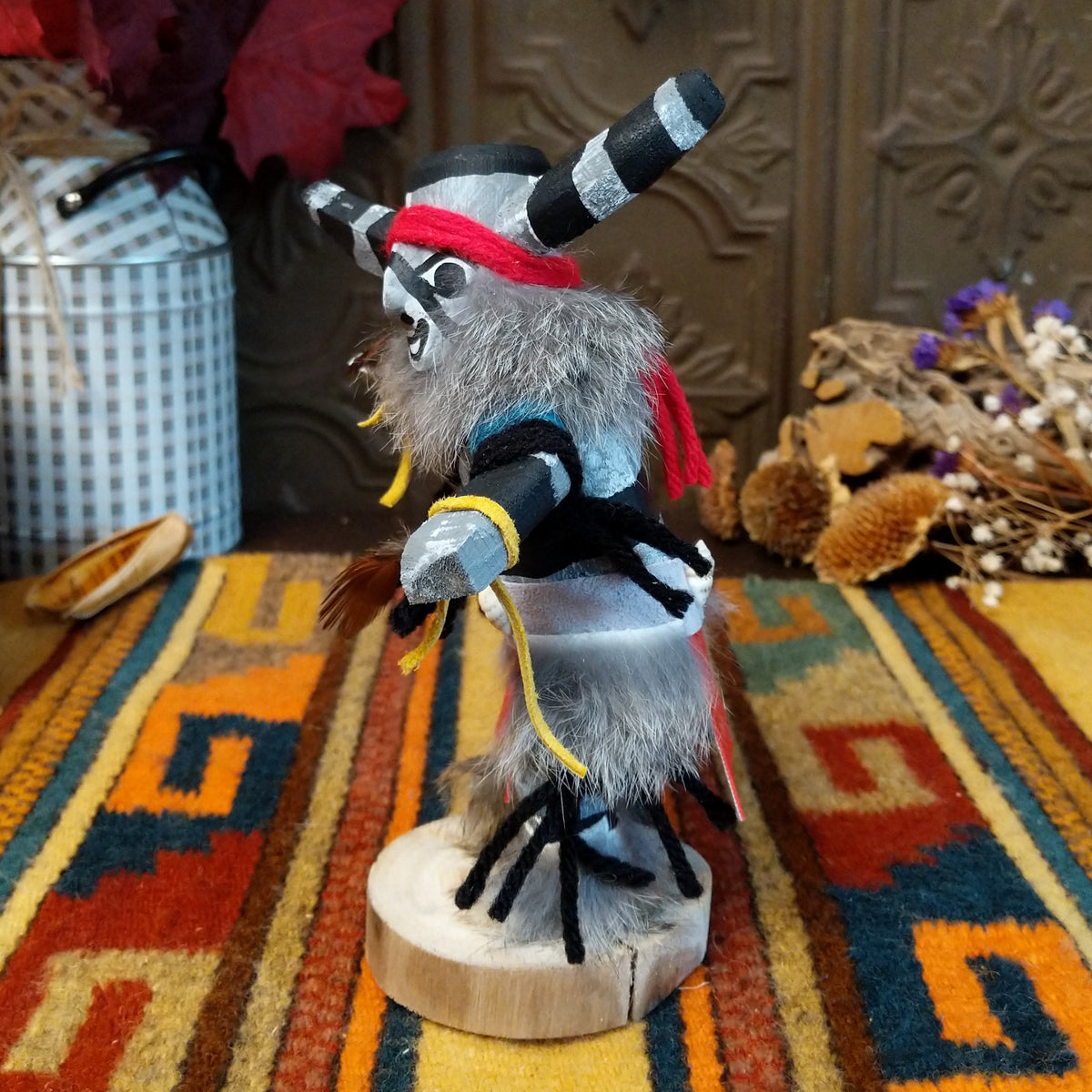 Side view of the Navajo Clown Kachina doll with black-and-silver striped horns, smiling painted face, gray fur, striped body, and red fabric apron.