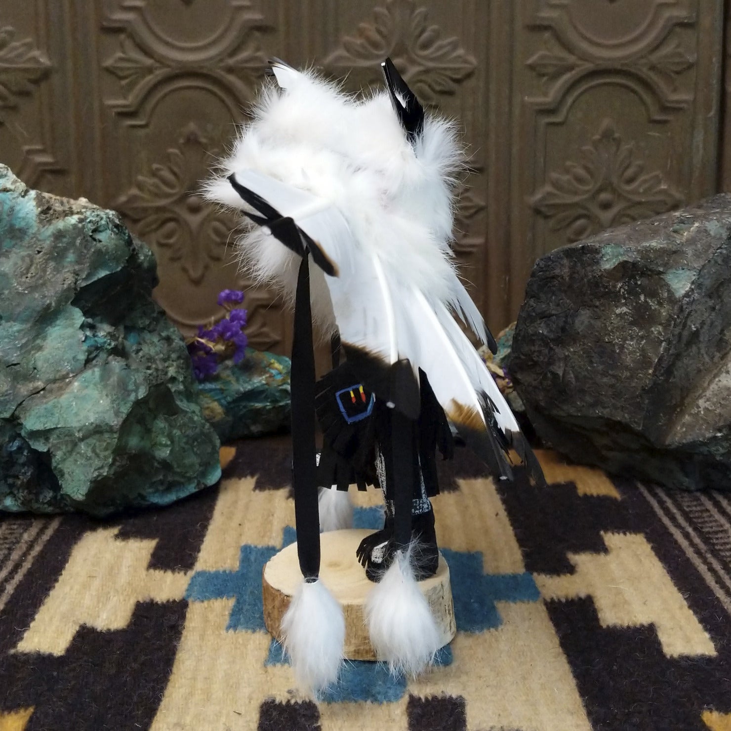 Navajo-made eagle kachina doll by M. C. with white feathered wings, blue mask, yellow beak, and black garments.