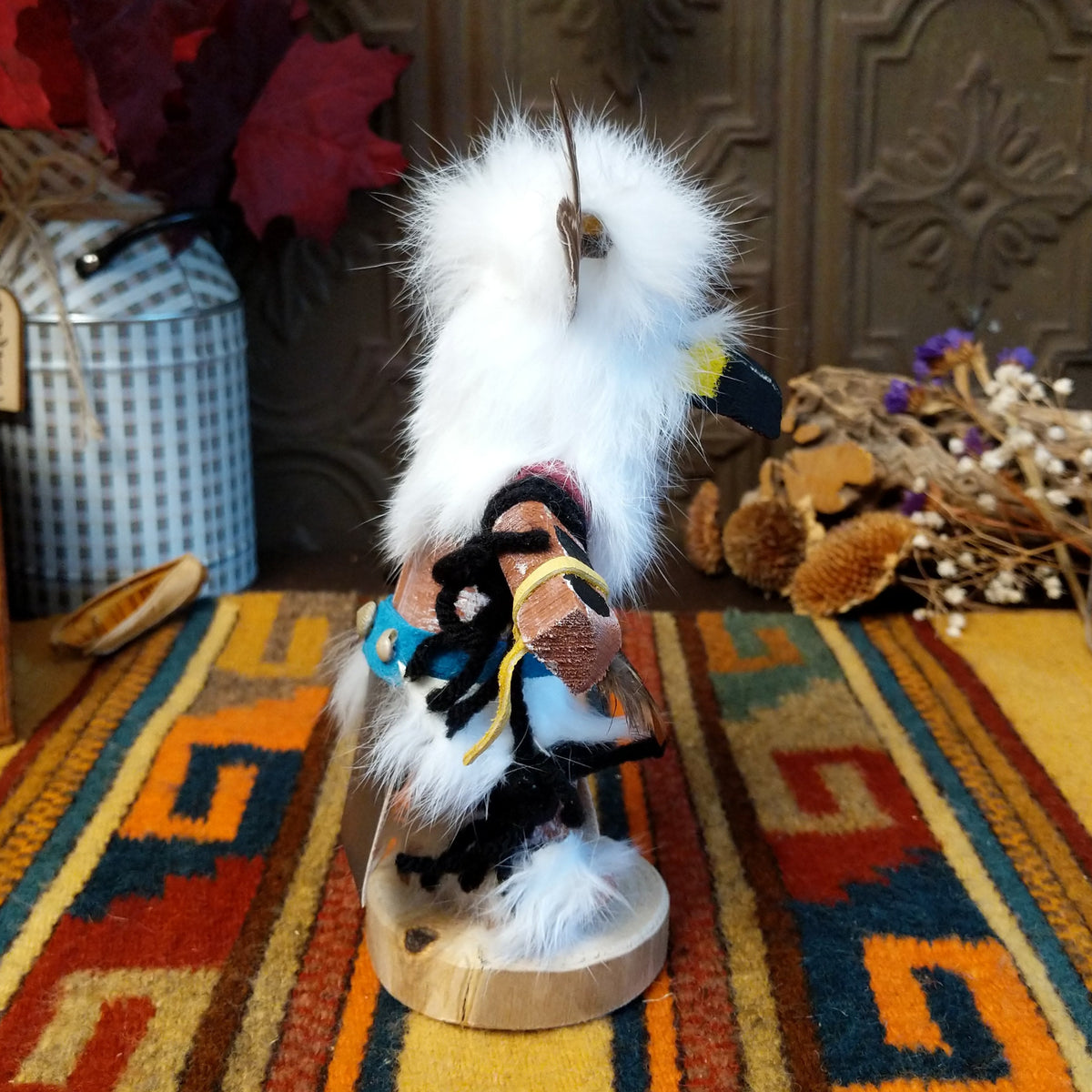 Side view of the Navajo Owl Kachina doll with fluffy white fur, black eyes, yellow-trimmed beak, brown feathers around the head, and blue belt.