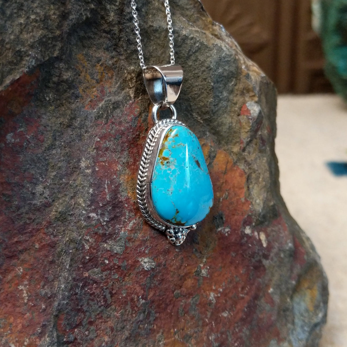 #8 turquoise pendant by Burt Francisco featuring a large teardrop-shaped blue turquoise stone with brown and golden matrix framed in twisted sterling silver; side view.