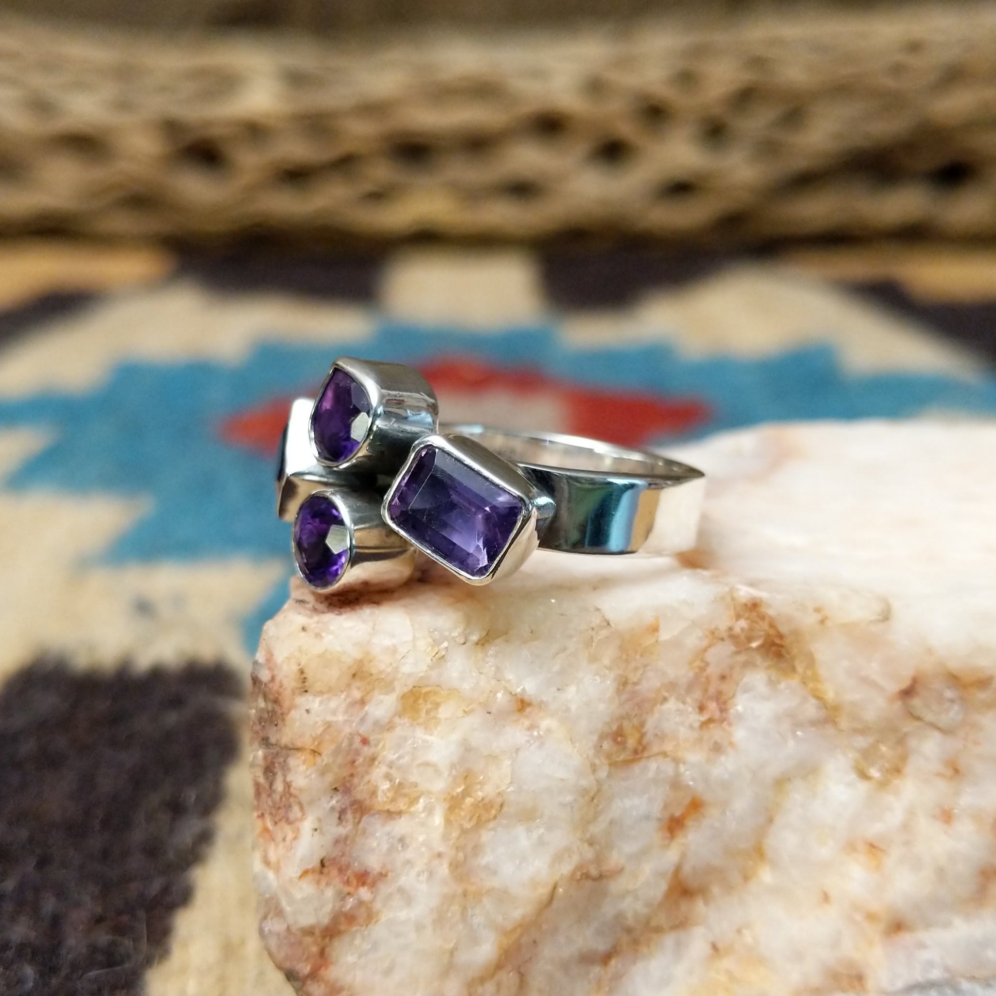 Amethyst ring by Ann Curley, featuring four faceted purple amethyst gemstones in round, square, rectangular, and pear shapes set in a handcrafted sterling silver ring. Side view.