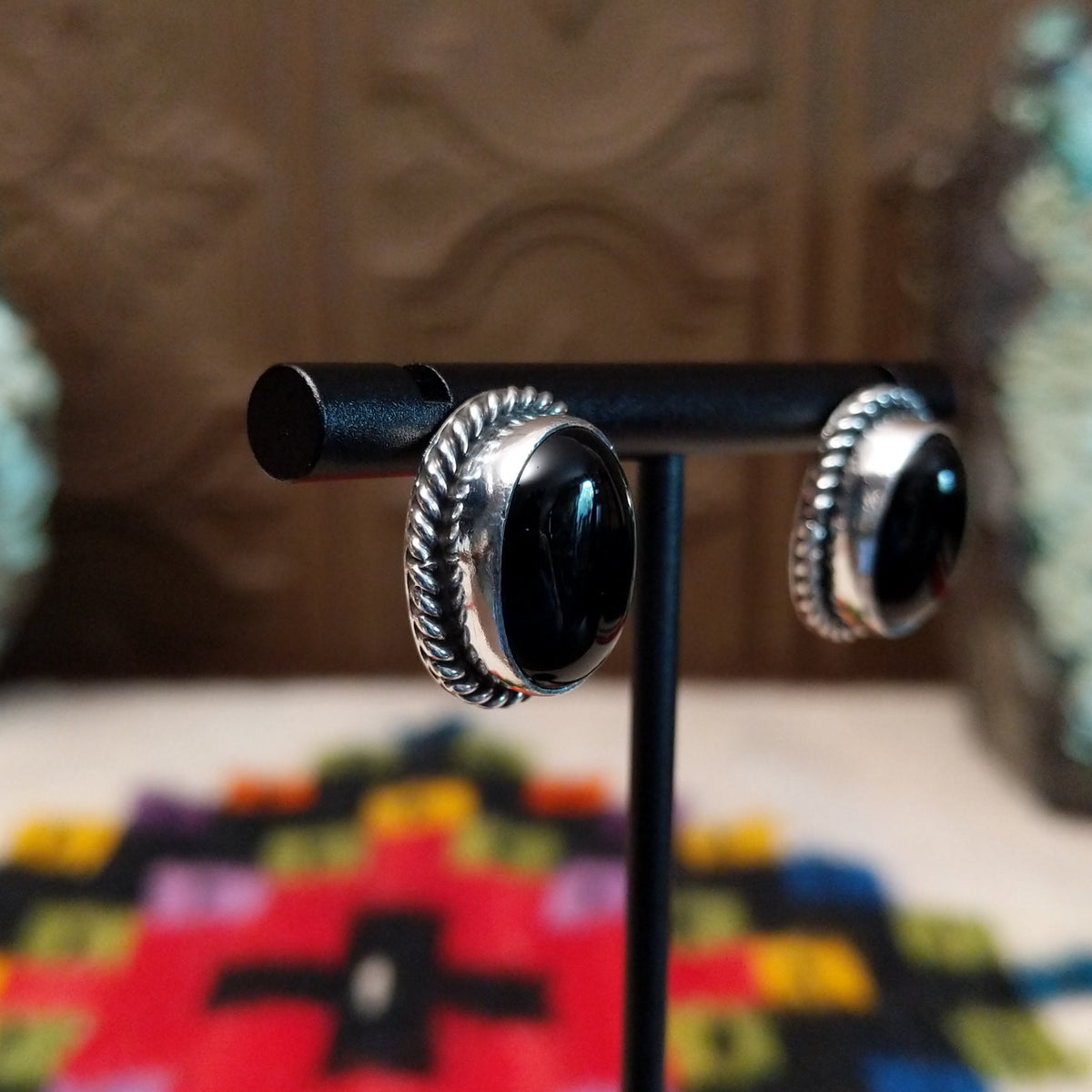 Black Onyx Oval Earrings by Priscilla Smith featuring glossy oval black onyx cabochons set in polished silver with detailed twisted rope-style borders; side view.
