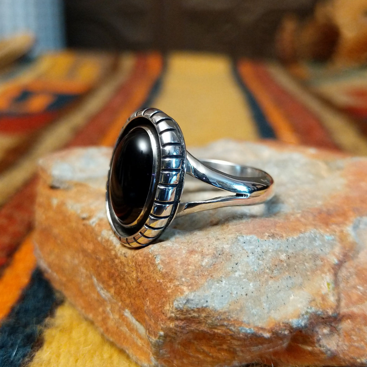 Angled view of a silver ring featuring an oval black onyx cabochon surrounded by a darkened recessed border, segmented silver detailing, and a polished split-shank band.