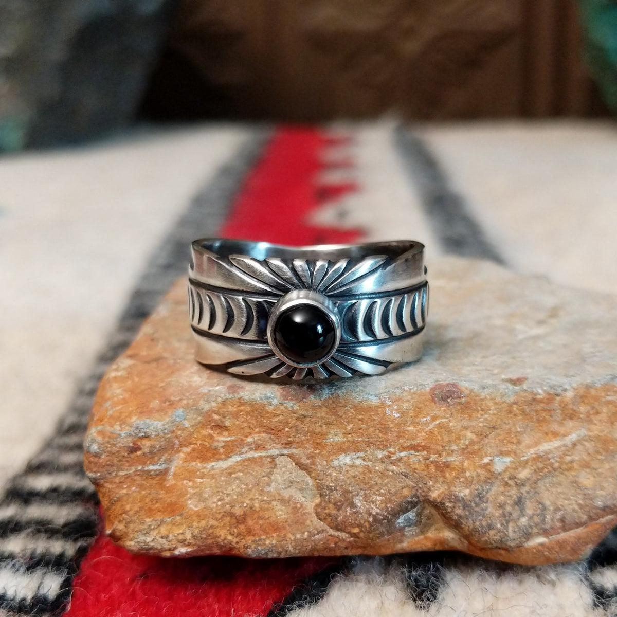Black Onyx ring by Raymond Coriz featuring a round polished black stone centered in a wide silver band with detailed stamped, radiating, and curved designs.