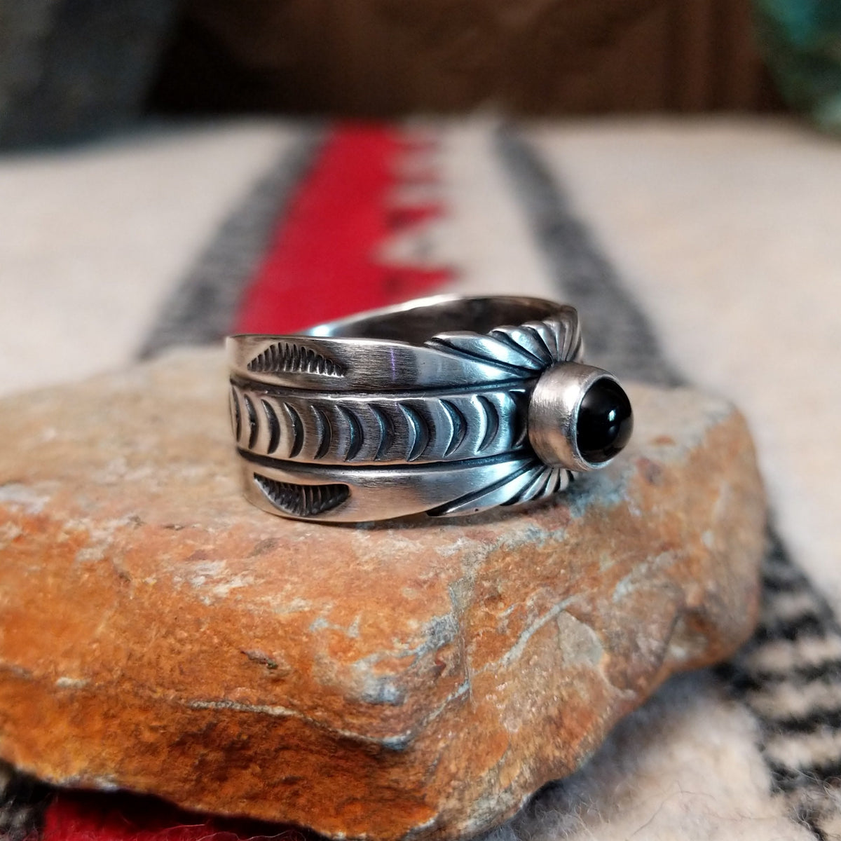 Black Onyx ring by Raymond Coriz featuring a round polished black stone centered in a wide silver band with detailed stamped, radiating, and curved designs; side view.