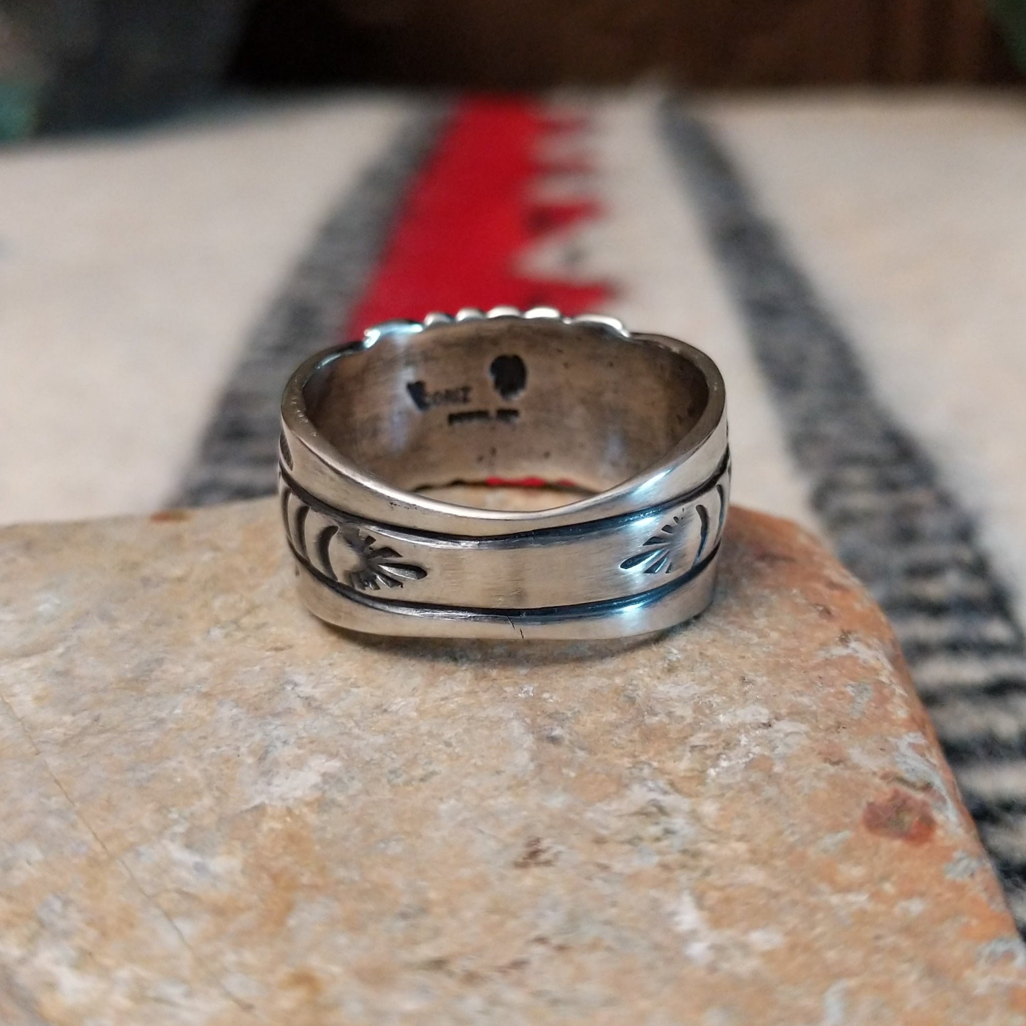 Black Onyx ring by Raymond Coriz featuring a round polished black stone centered in a wide silver band with detailed stamped, radiating, and curved designs; underside view.