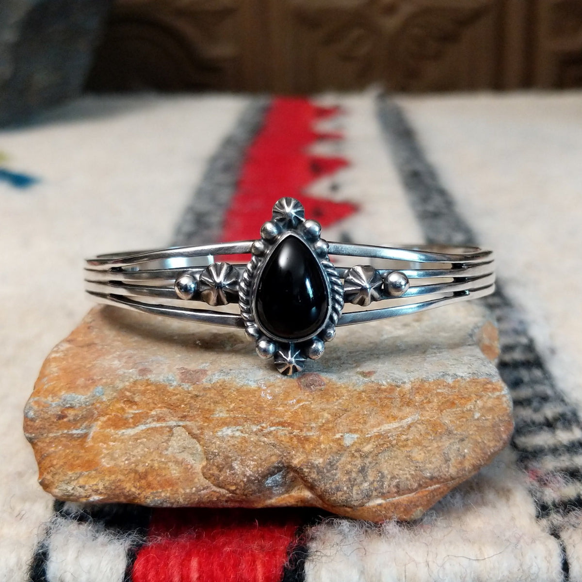Silver cuff by Raymond Coriz featuring a polished teardrop-shaped black onyx surrounded by twisted wire, silver drops, stamped accents, and layered silver bands.
