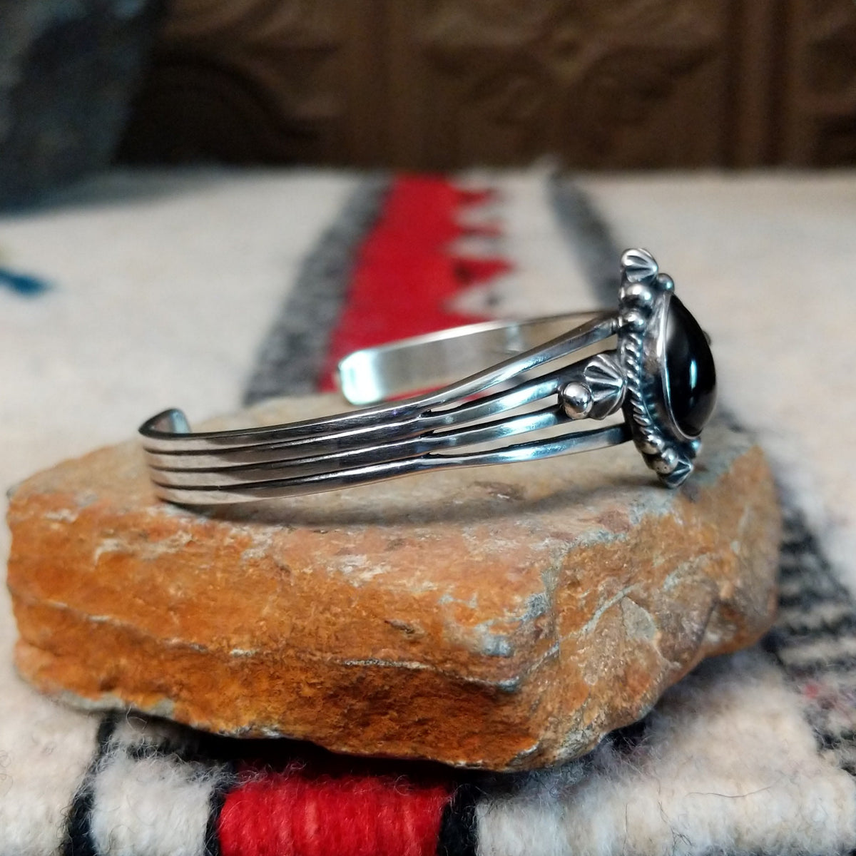 Silver cuff by Raymond Coriz featuring a polished teardrop-shaped black onyx surrounded by twisted wire, silver drops, stamped accents, and layered silver bands; side view.