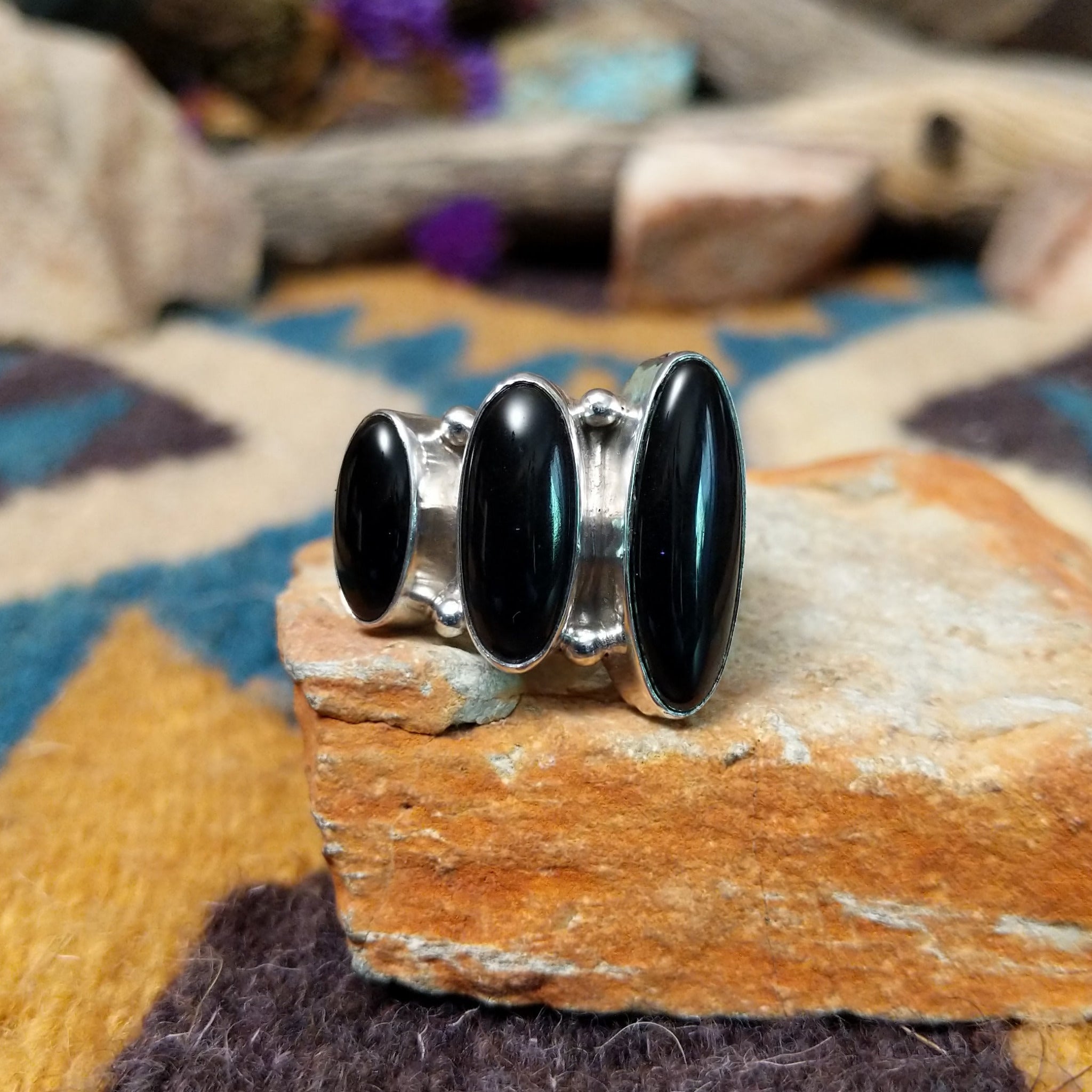 Handcrafted Navajo sterling silver ring by Ann Curley featuring three graduated oval black onyx cabochons in bezel settings with polished silver bead accents on a wide statement band.
