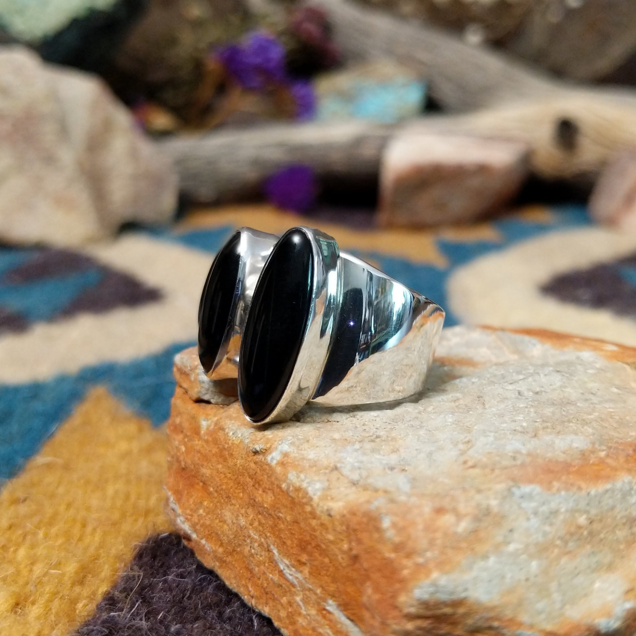 Handcrafted Navajo sterling silver ring by Ann Curley featuring three graduated oval black onyx cabochons in bezel settings with polished silver bead accents on a wide statement band; side view.