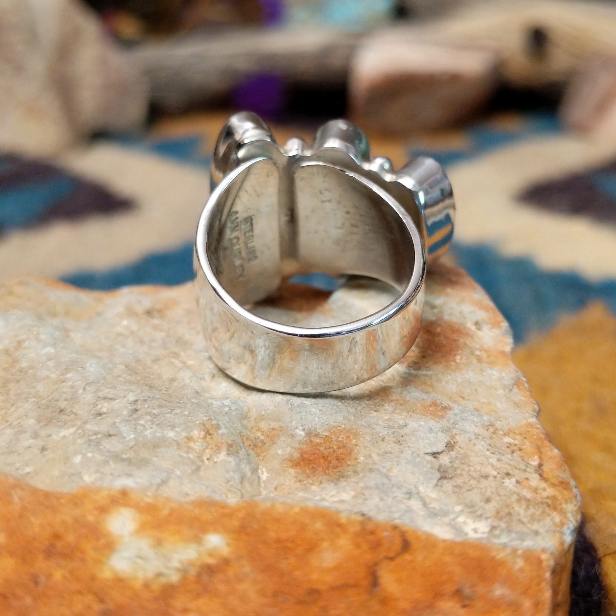 Handcrafted Navajo sterling silver ring by Ann Curley featuring three graduated oval black onyx cabochons in bezel settings with polished silver bead accents on a wide statement band; underside view.