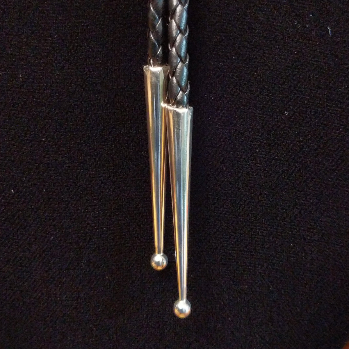 This striking Bumblebee Jasper Bolo Tie by Terry Wood features a bright yellow oval stone with gray and black matrix, a decorative stamped silver setting, braided black leather cord, and polished silver tips; tips close-up view.