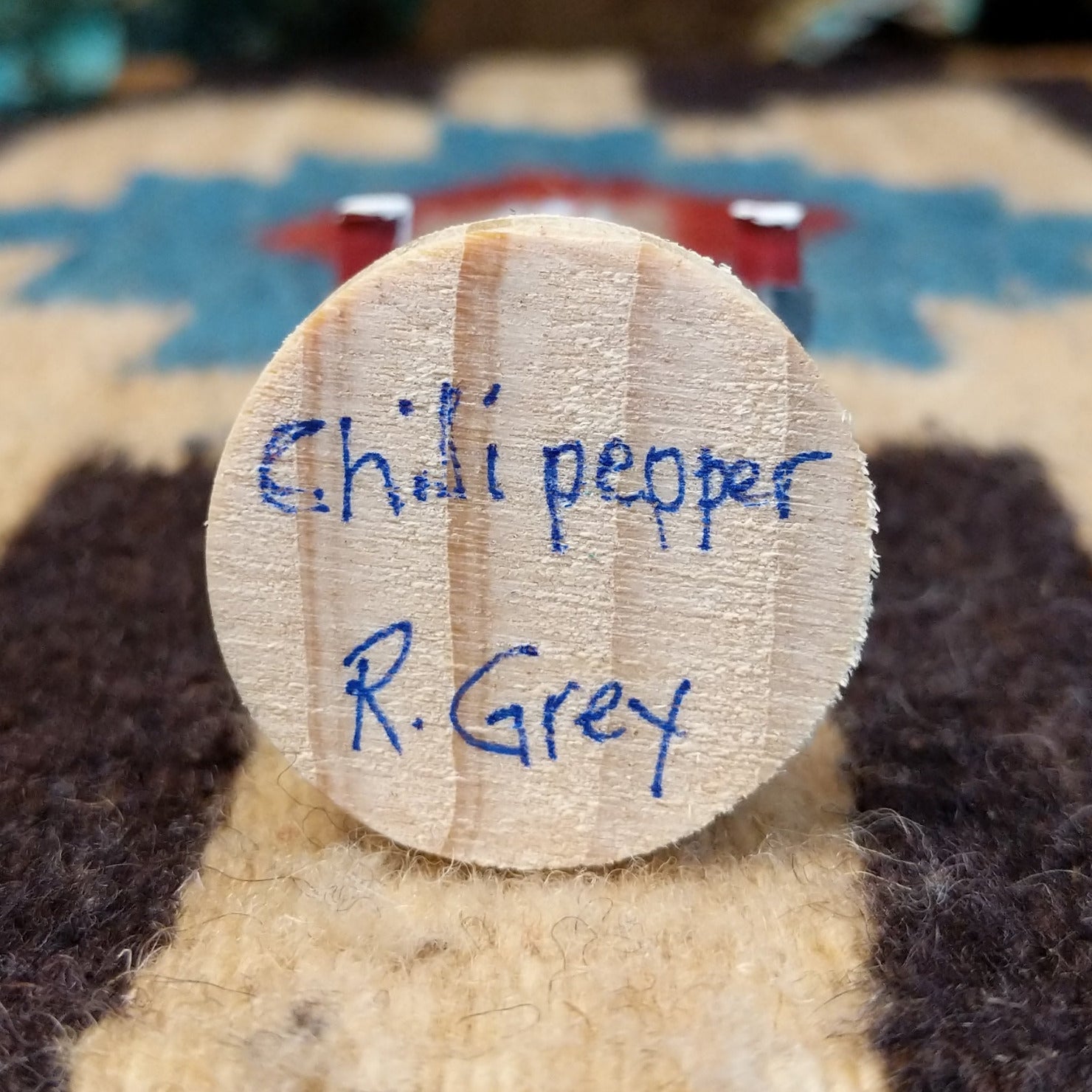 Underside of chili pepper mini kachina doll showing handwritten signature and label on wood base.