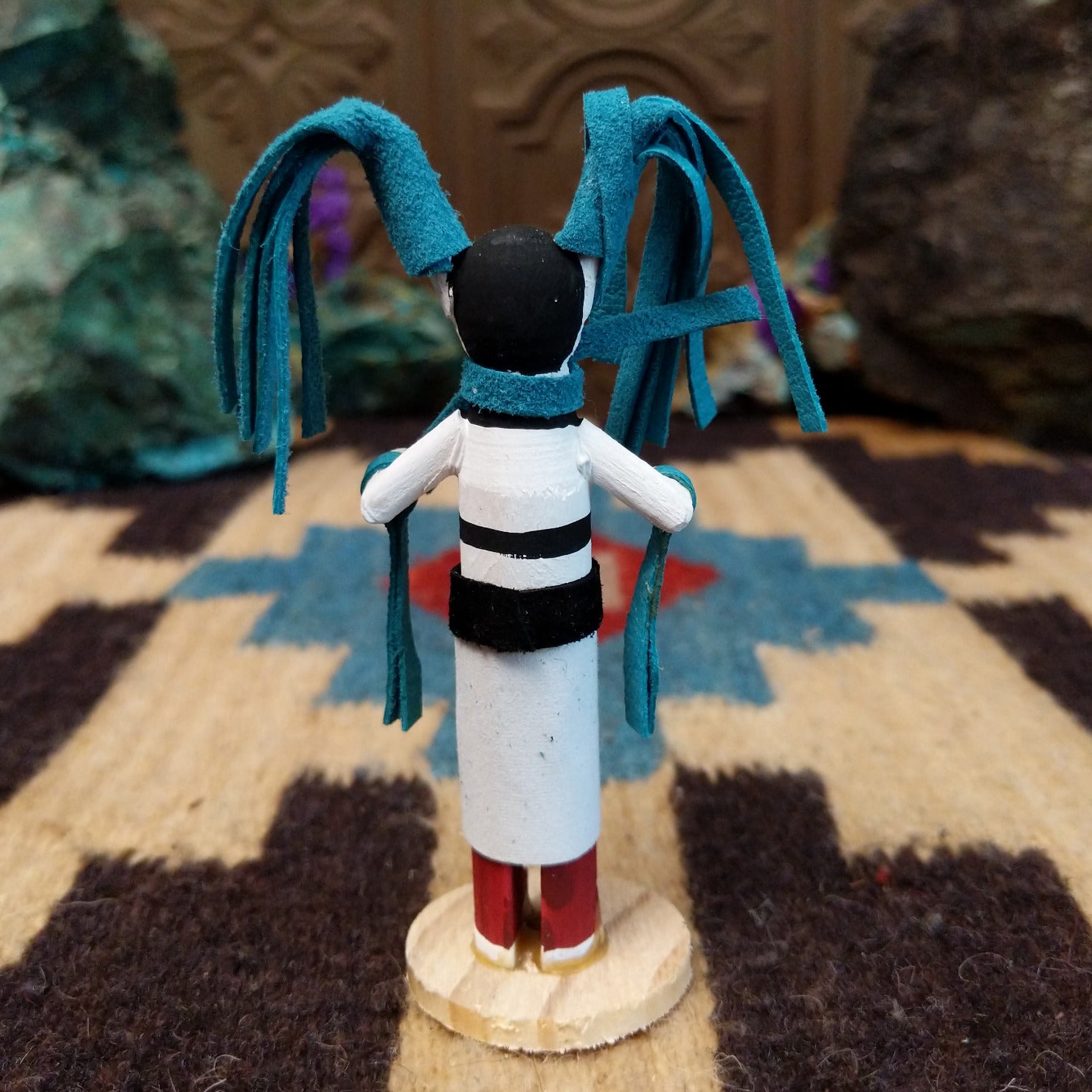 Mini clown kachina by Rosalind Grey with turquoise pigtails, white face, black striped body, and white geometric-patterned garment.