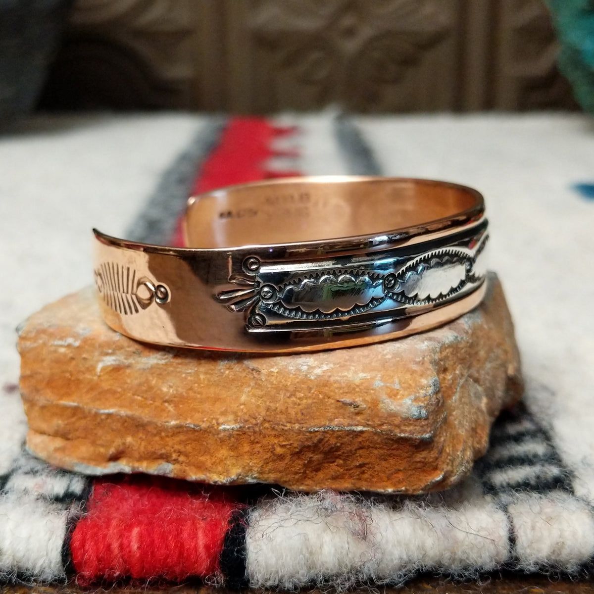 This Copper & Silver Cuff by Robert Little features polished copper borders, a sterling silver center, repeating scalloped hand-stamped motifs, fine textured edges, and dark oxidized accents; side view.