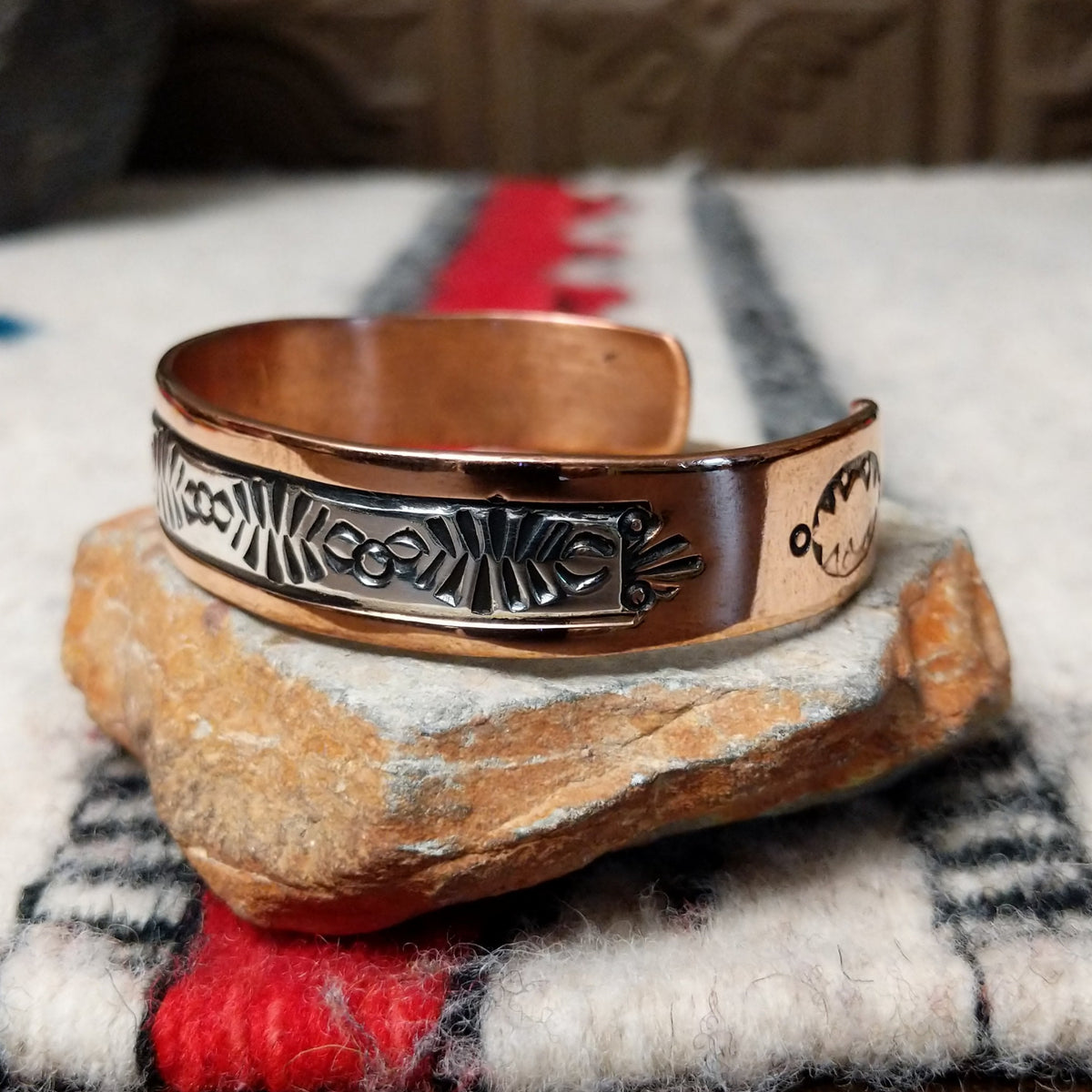 Copper and silver cuff by Robert Little featuring an intricate repeating hand-stamped geometric pattern with oxidized accents, framed by polished copper borders; side view.