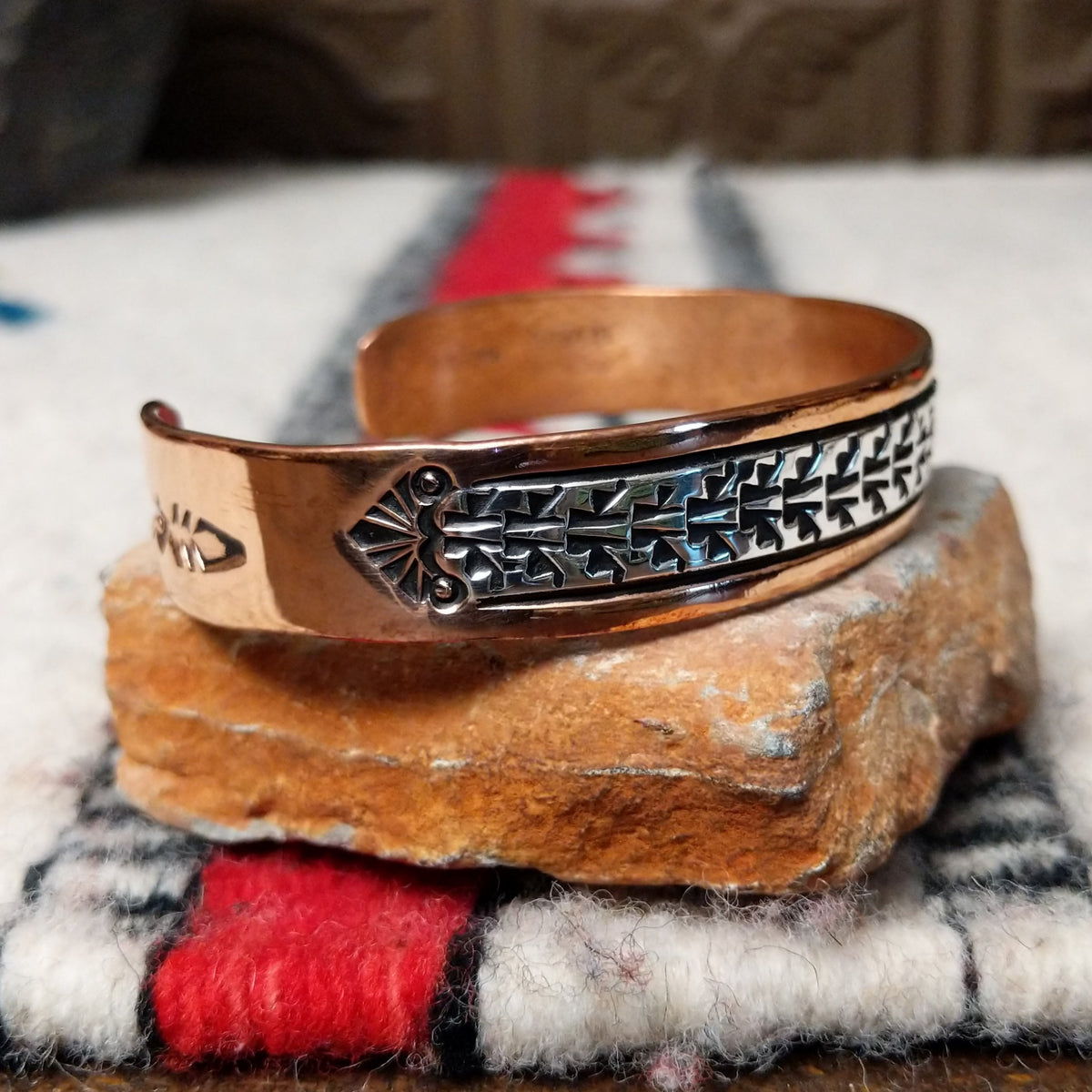 Copper and silver cuff by Robert Little featuring a repeating stepped geometric pattern in oxidized sterling silver, framed by polished copper borders; side view.