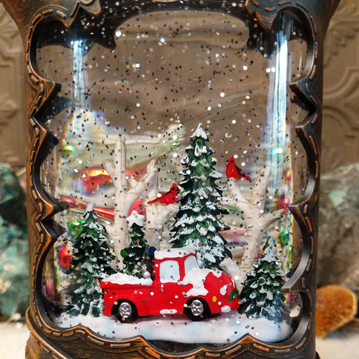 Festive Cowboy Boot Truck Snow Globe featuring a red vintage pickup truck surrounded by snow-covered trees inside a dark brown Western boot with silver stars and concho detailing.
