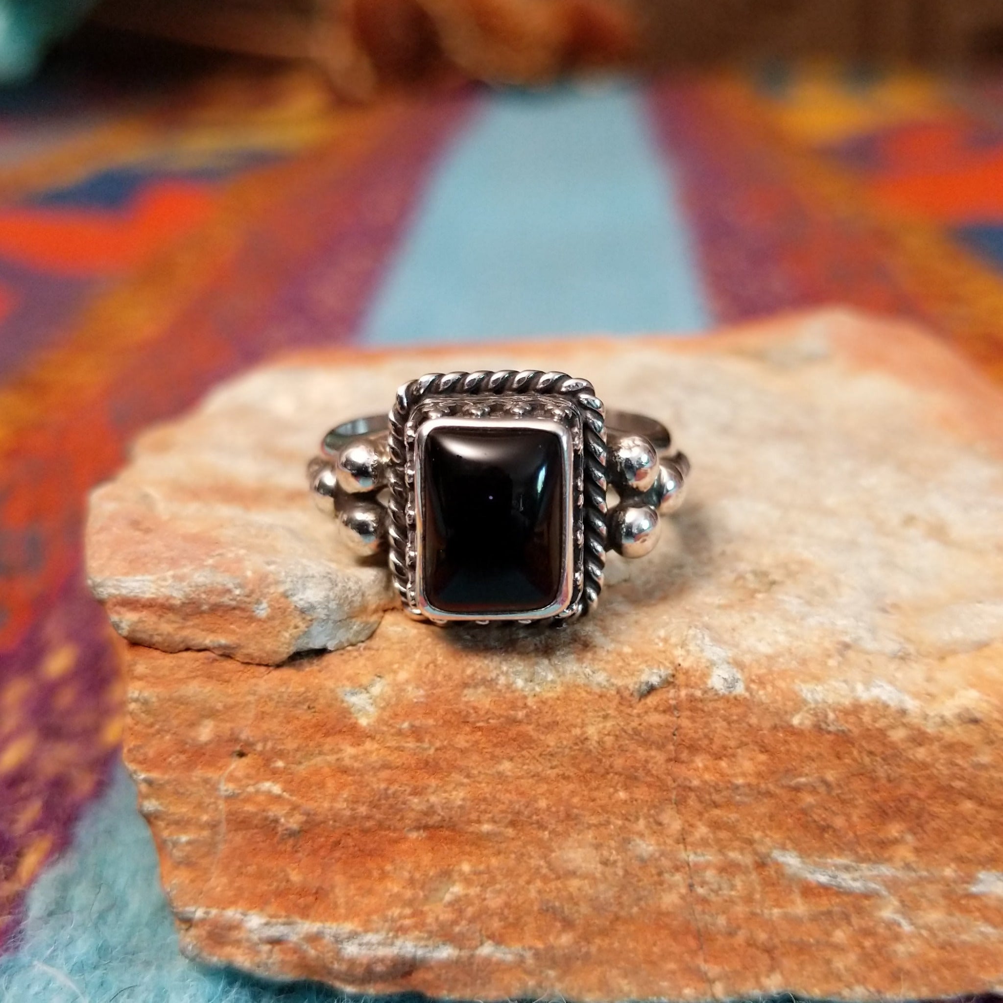 Black onyx silver ring by Angela Martin with twisted border and silver drop accents.