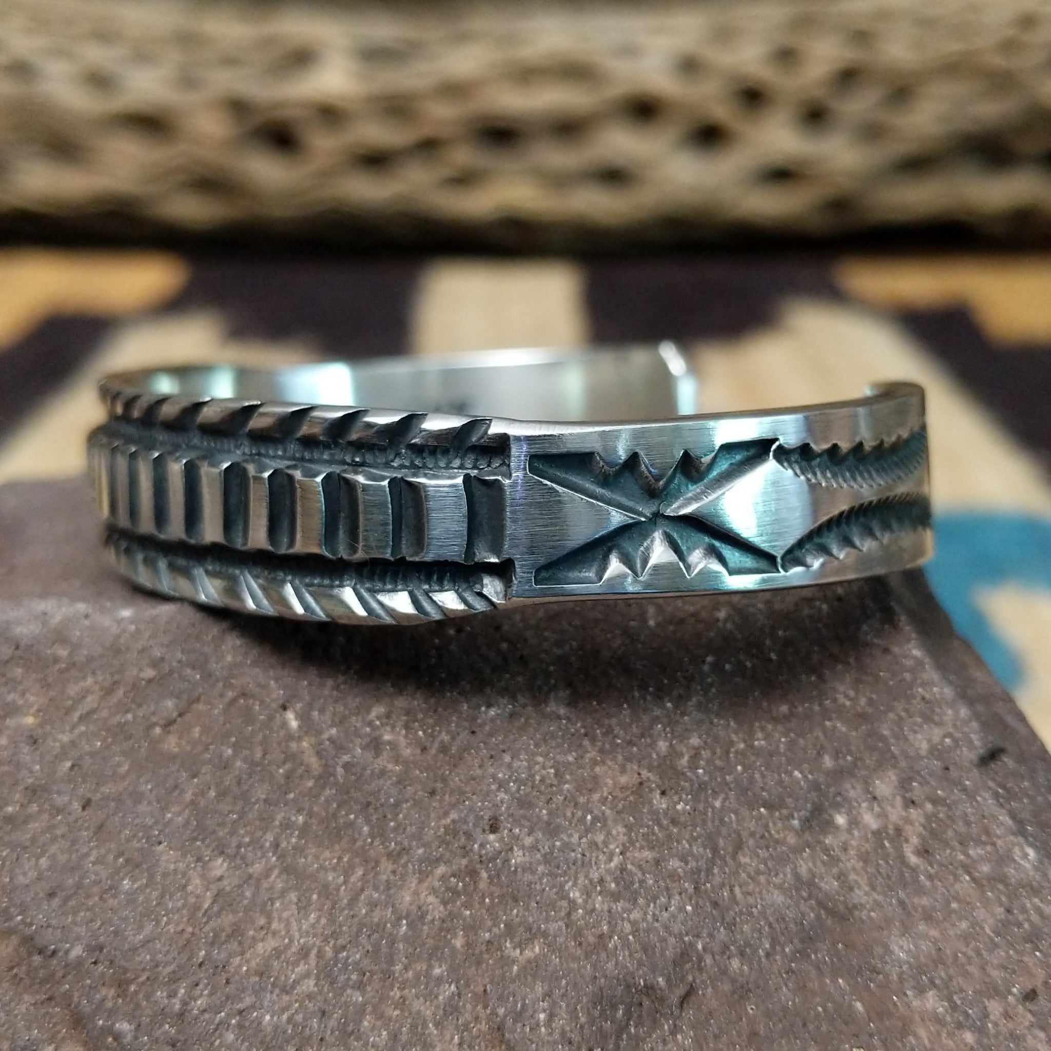 Deep stamped sterling silver cuff by Jerrold Tahe, featuring bold hand-stamped patterns with deep texture on a handcrafted open sterling silver cuff. Side view.