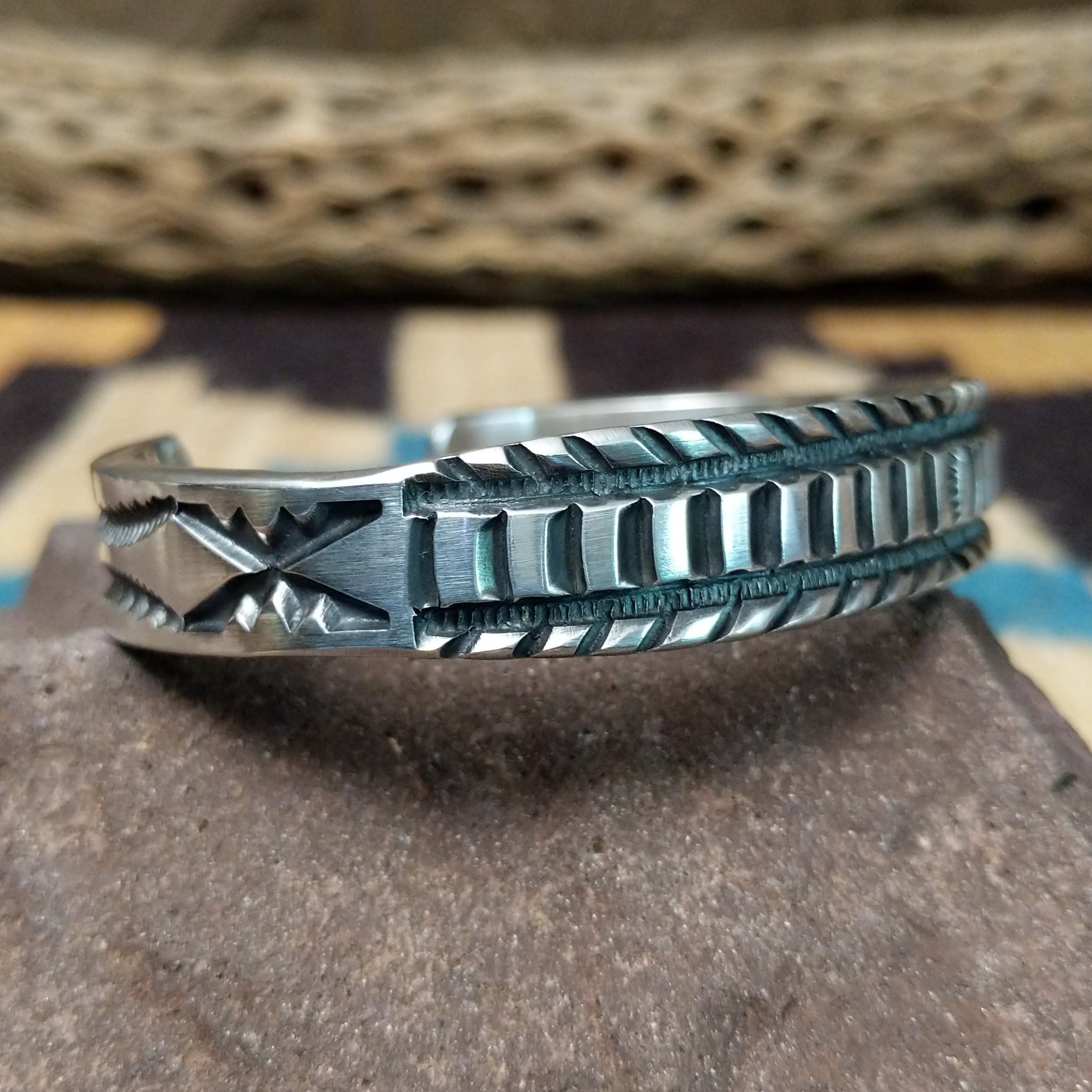 Deep stamped sterling silver cuff by Jerrold Tahe, featuring bold hand-stamped patterns with deep texture on a handcrafted open sterling silver cuff. Side view.