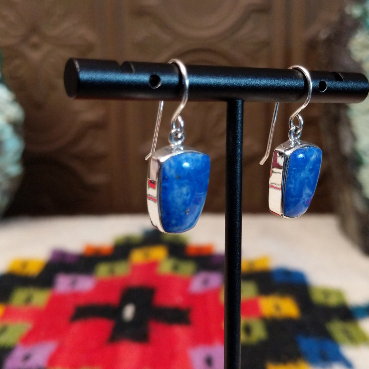 Denim Lapis Earrings by Cathy Webster featuring polished blue stones with cloudy light-blue and white variations, set in smooth silver bezels and suspended from French ear wires; side view.