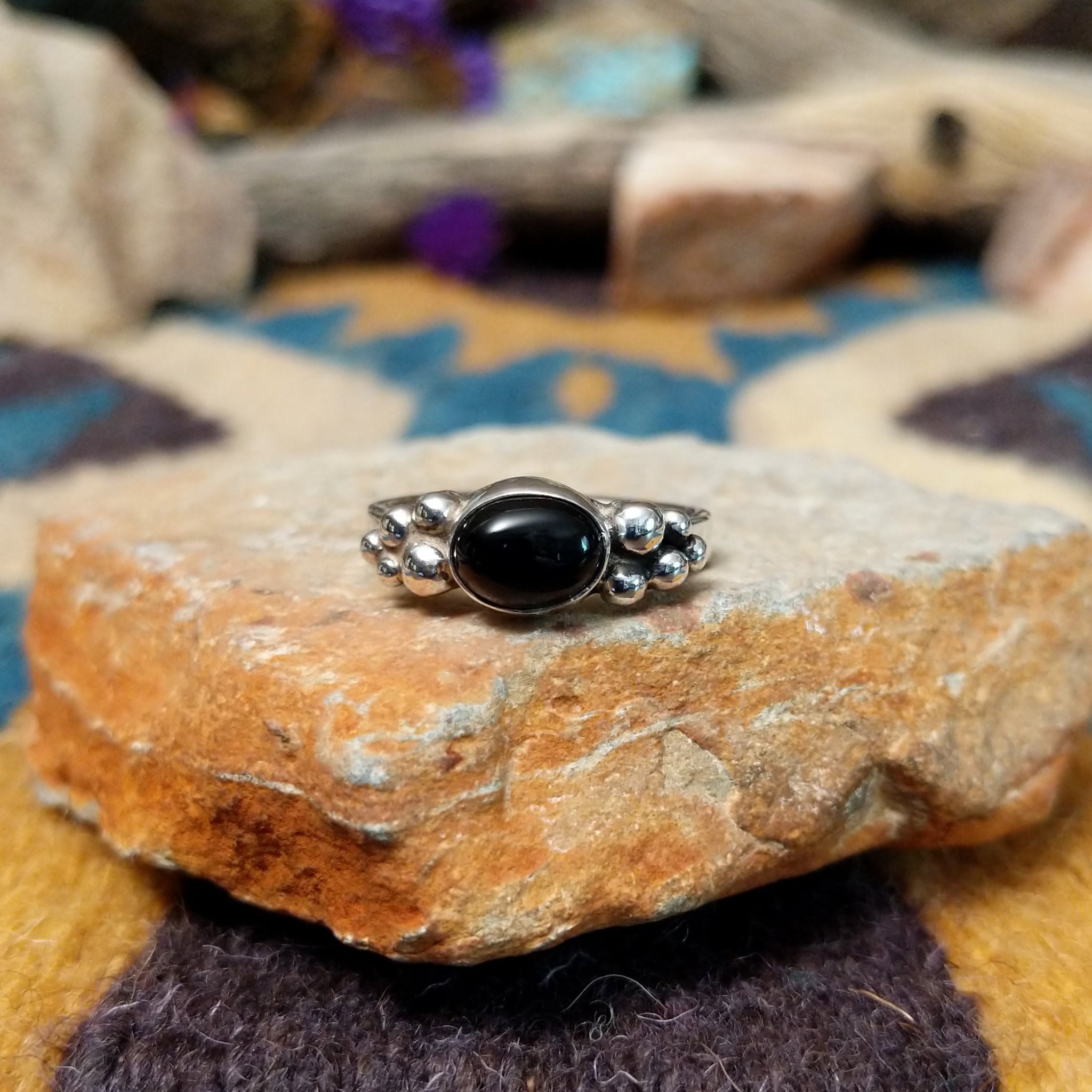 Handcrafted sterling silver Navajo ring featuring a polished oval Black Onyx cabochon in a smooth bezel setting, accented by decorative sterling silver bead clusters on each side of the gemstone.