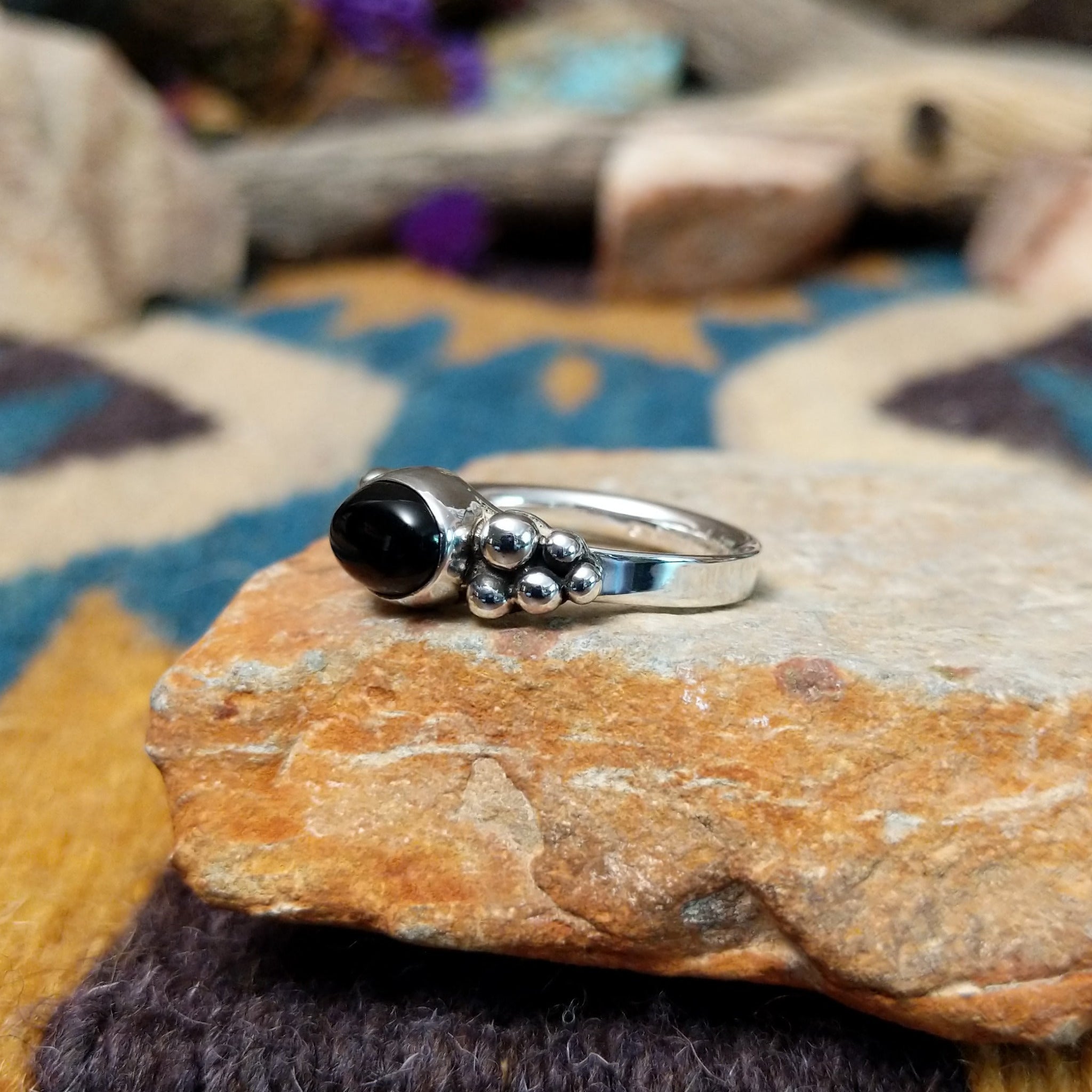Handcrafted sterling silver Navajo ring featuring a polished oval Black Onyx cabochon in a smooth bezel setting, accented by decorative sterling silver bead clusters on each side of the gemstone; side view.