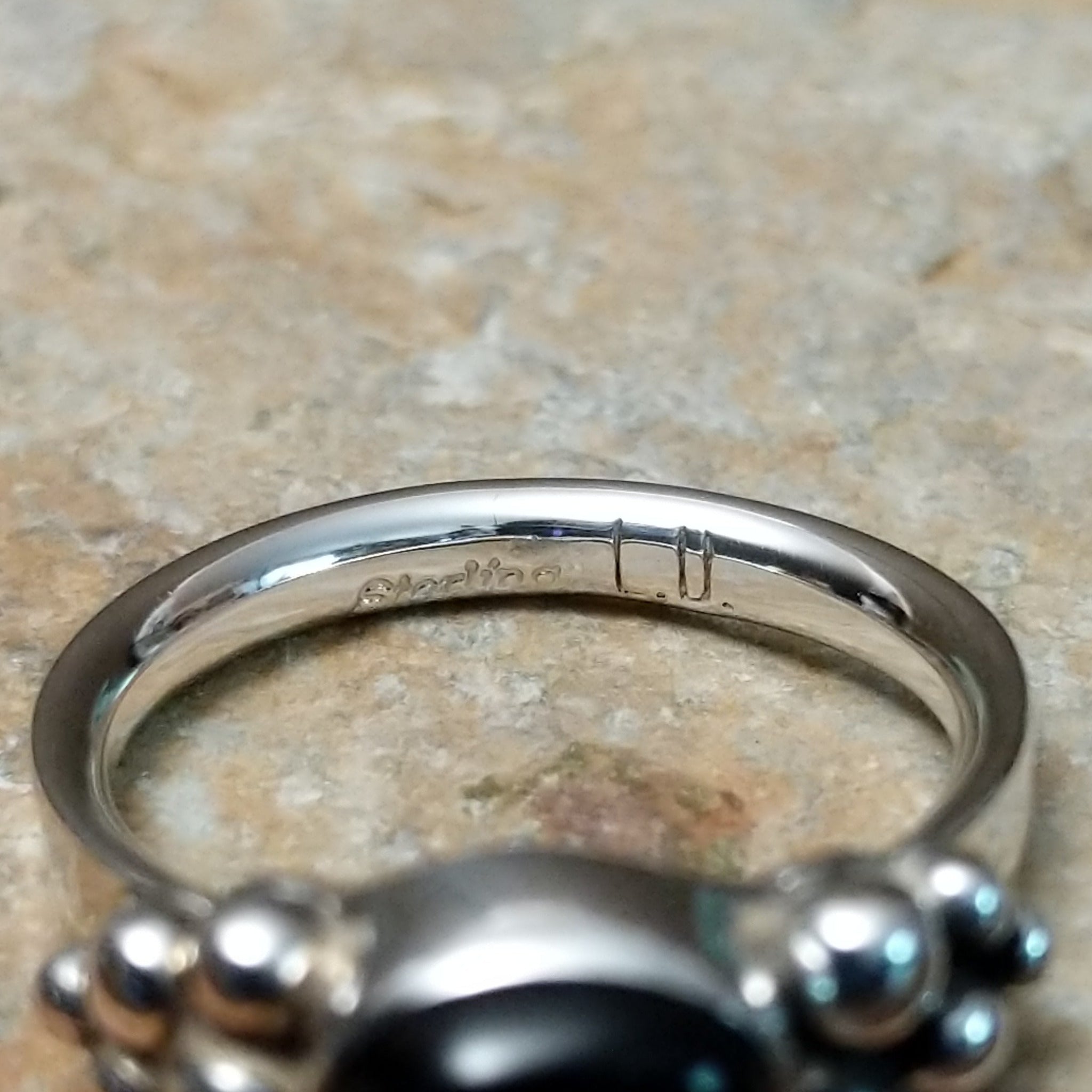 Handcrafted sterling silver Navajo ring featuring a polished oval Black Onyx cabochon in a smooth bezel setting, accented by decorative sterling silver bead clusters on each side of the gemstone; artisan and Sterling Silver stamp.