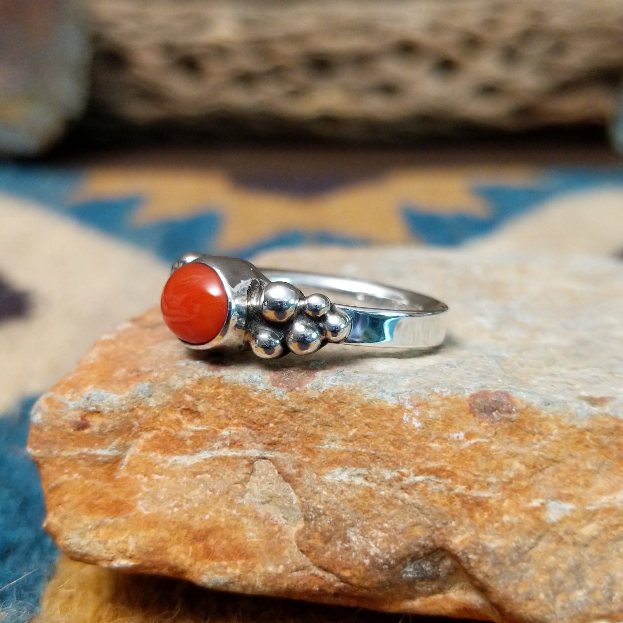 Handcrafted sterling silver dotted coral ring by Lowell Draper, featuring an oval coral cabochon with polished silver bead accents; side view.