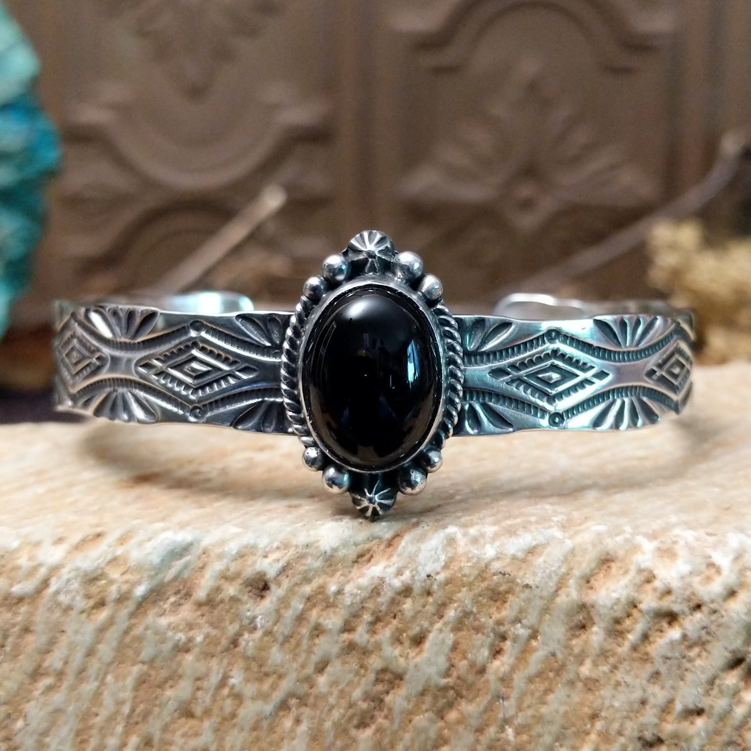 Sterling silver cuff bracelet with black onyx set in the oval bezel, framed by twisted rope and dotted accents while the band features abstract stamping.