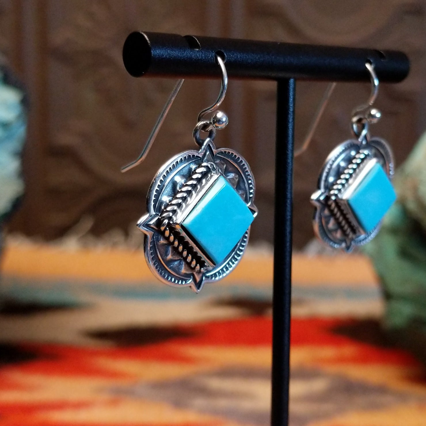 Sterling silver earrings with Kingman turquoise set in diamond-shaped bezels, framed by ornate stamped settings.