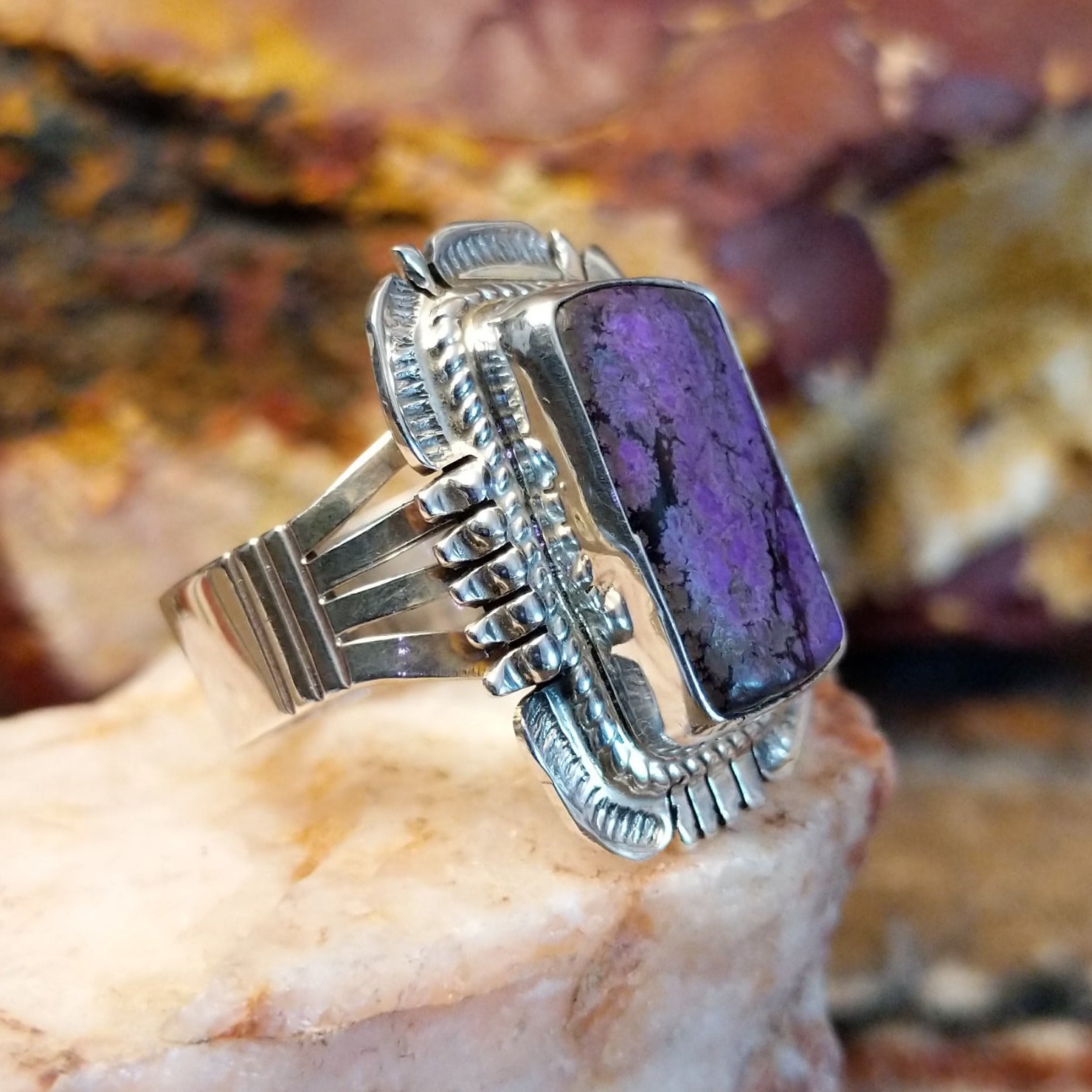 Square sugilite ring set within an intricate silver work bezel.
