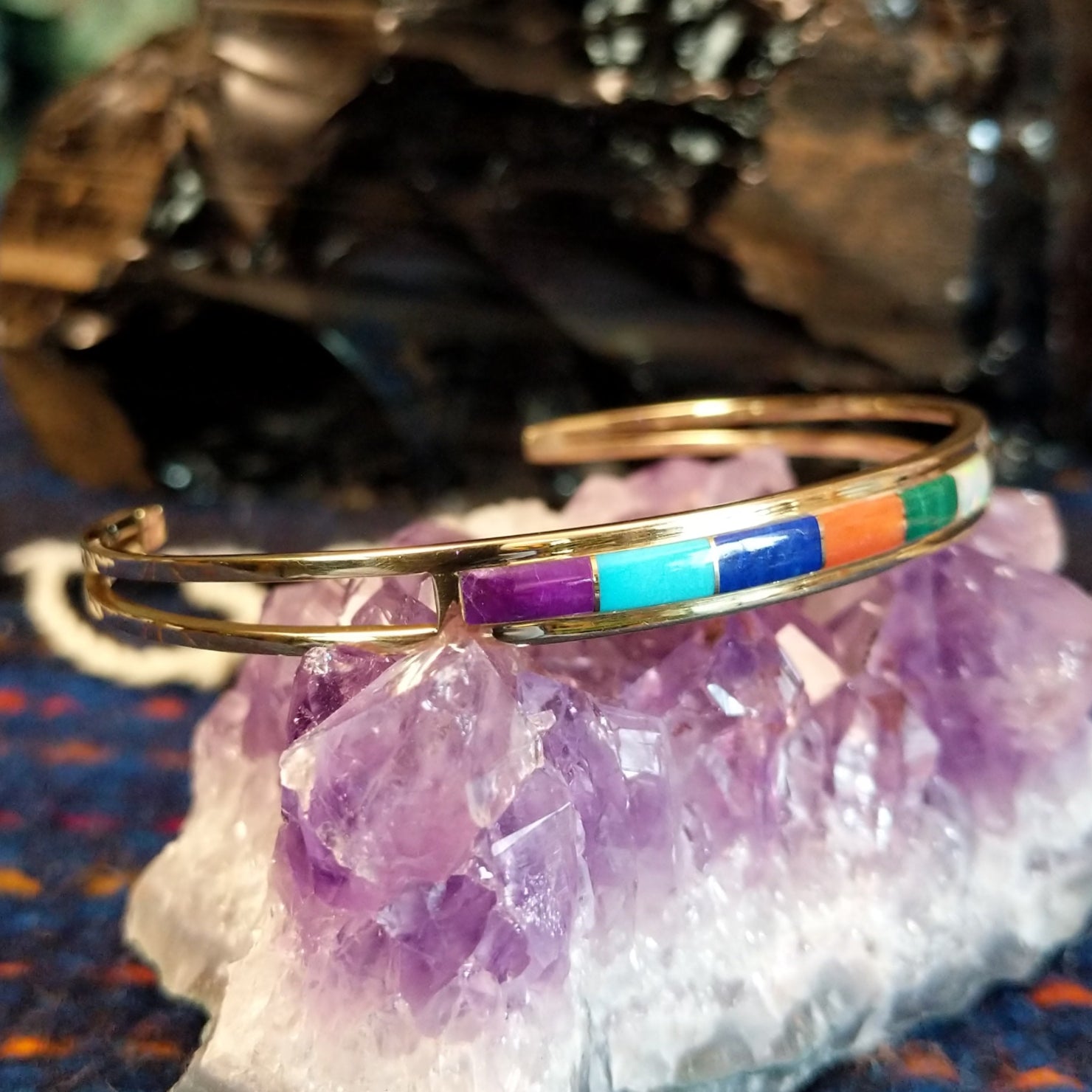 Gold cuff bracelet featuring a vibrant, multi-stone inlay set in a polished gold frame.