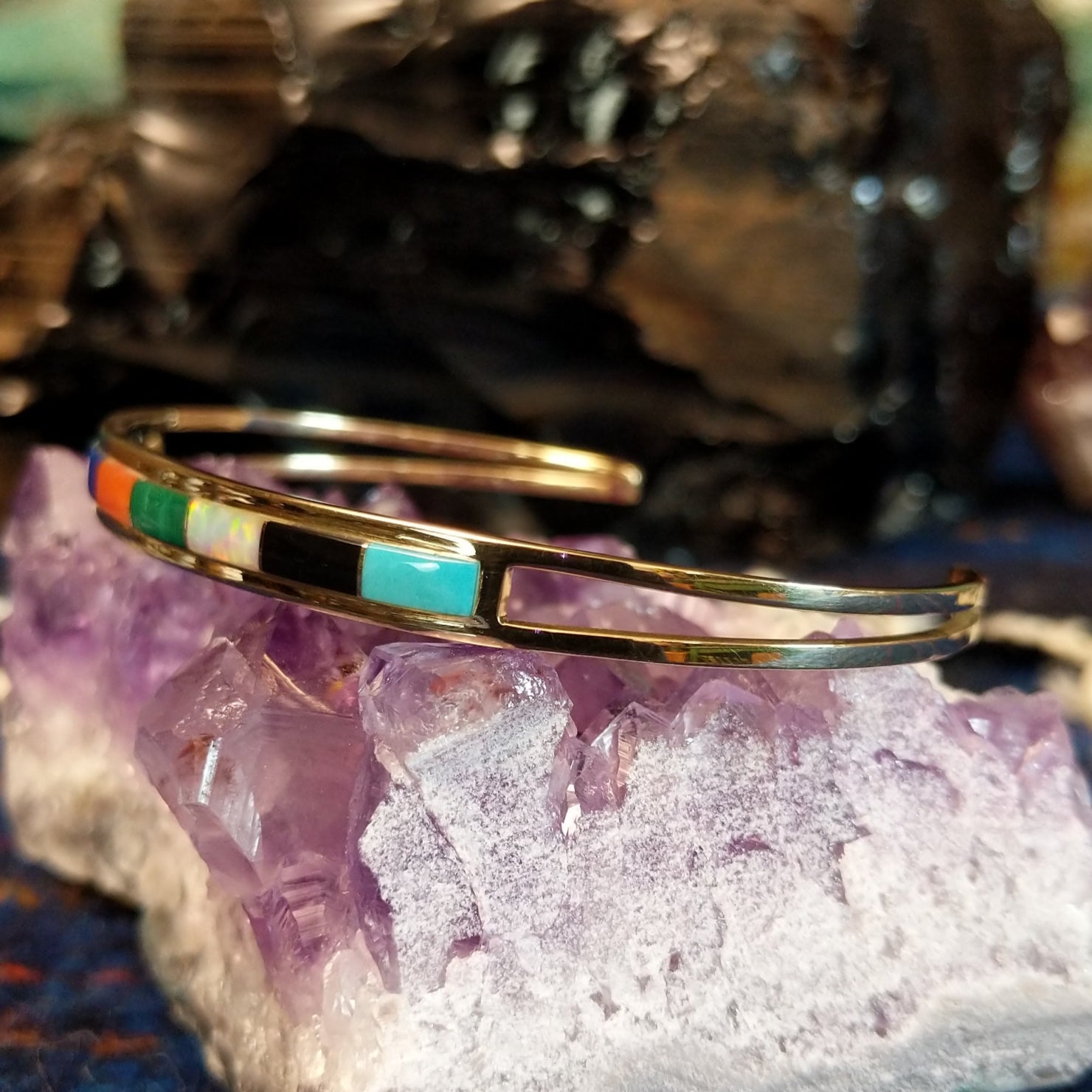 Gold cuff bracelet featuring a vibrant, multi-stone inlay set in a polished gold frame.