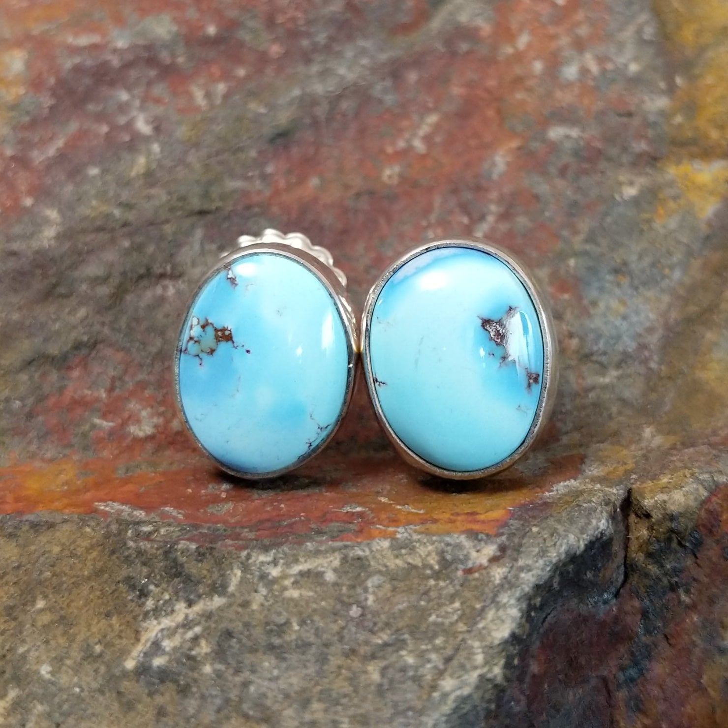 The front view of the golden hills turquoise oval earrings by Diane Wylie features vibrant turquoise stones with a brown matrix, set in a simple silver bezel.