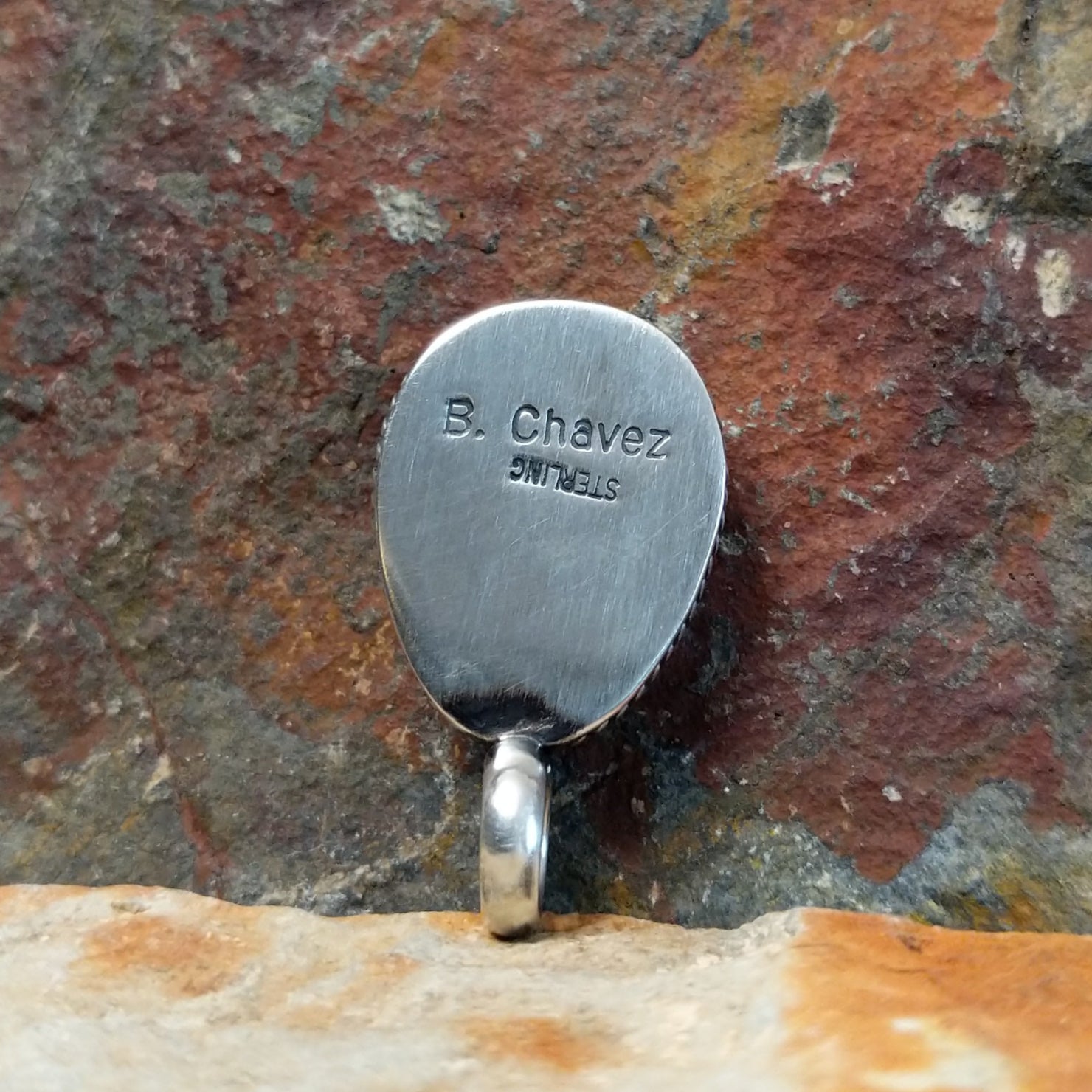 The stamped view of this turquoise pendant displays a maker’s mark etched into the silver bezel.