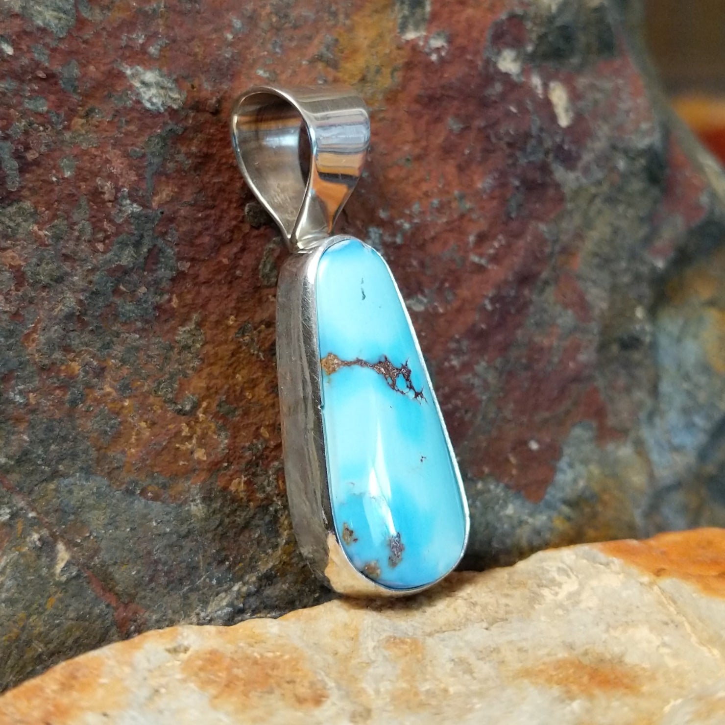 The side of this turquoise pendant reveals a polished silver base with a simple bail at the top.