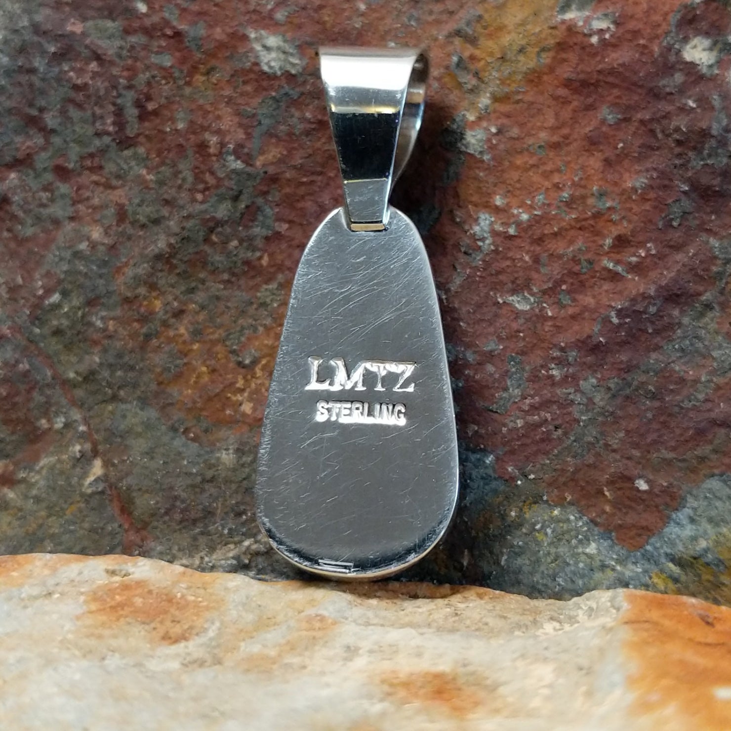The stamped view of this turquoise pendant reveals a maker’s mark etched into the silver base near the smooth bezel.