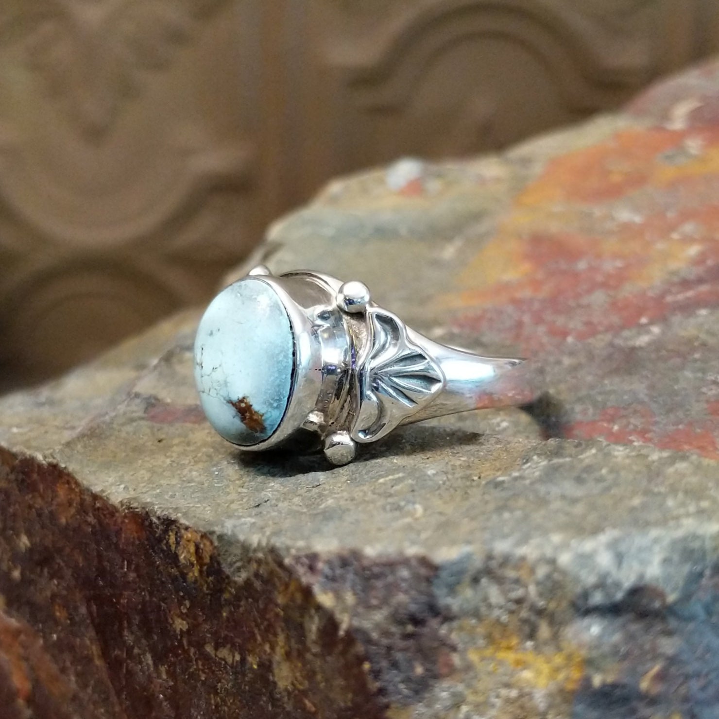 Silver ring with a smooth bezel holding a round turquoise stone with silver accents along the bezel and band.