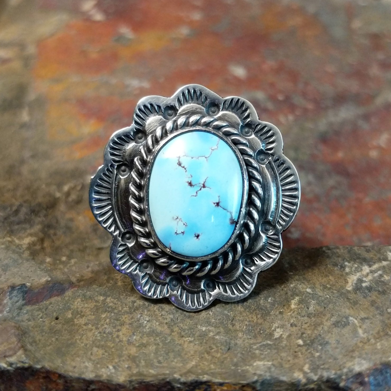 Silver ring with a large oval turquoise stone in a smooth bezel. Twisted rope and scalloped edge surround the stone with matrix veining.