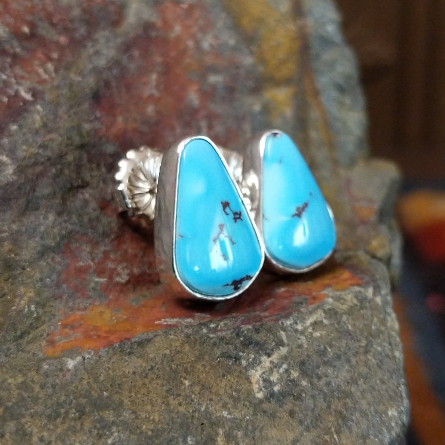 A side view of the golden hills turquoise triangular earrings by Diane Wylie shows the turquoise stone’s smooth edge in a simple bezel. The silver post shines against the stone’s vivid blue.