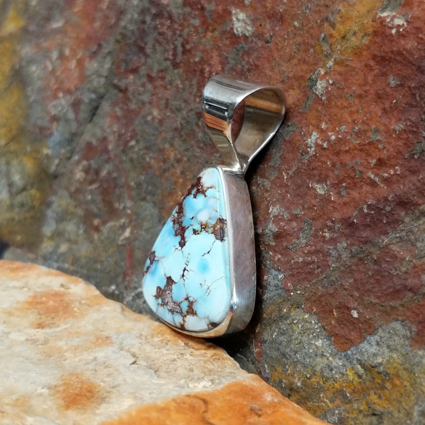 A side view reveals the triangular turquoise stone’s brown matrix in a simple silver bezel, with the silver bail shining.