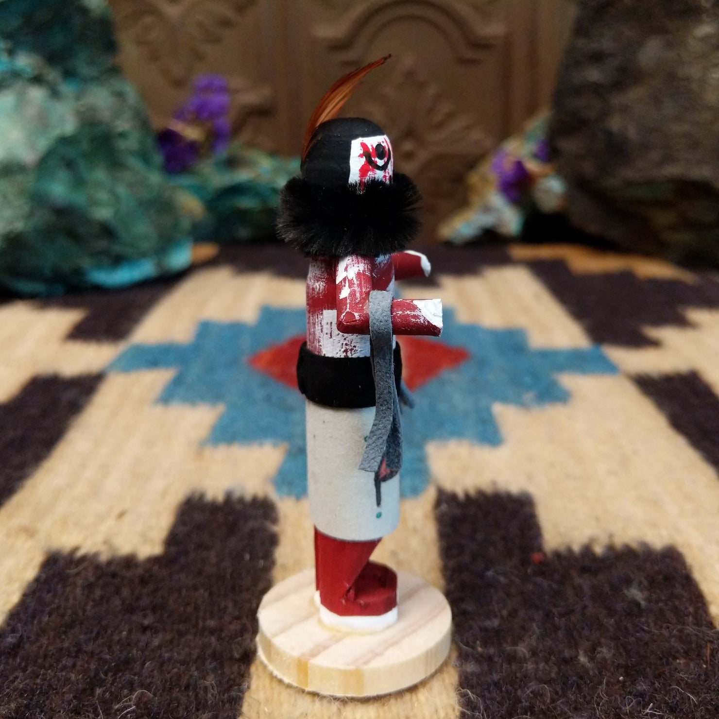 Mini grandmother kachina by Rosalind Grey with red body, black fur collar, feathered headpiece, and white geometric-patterned garment.