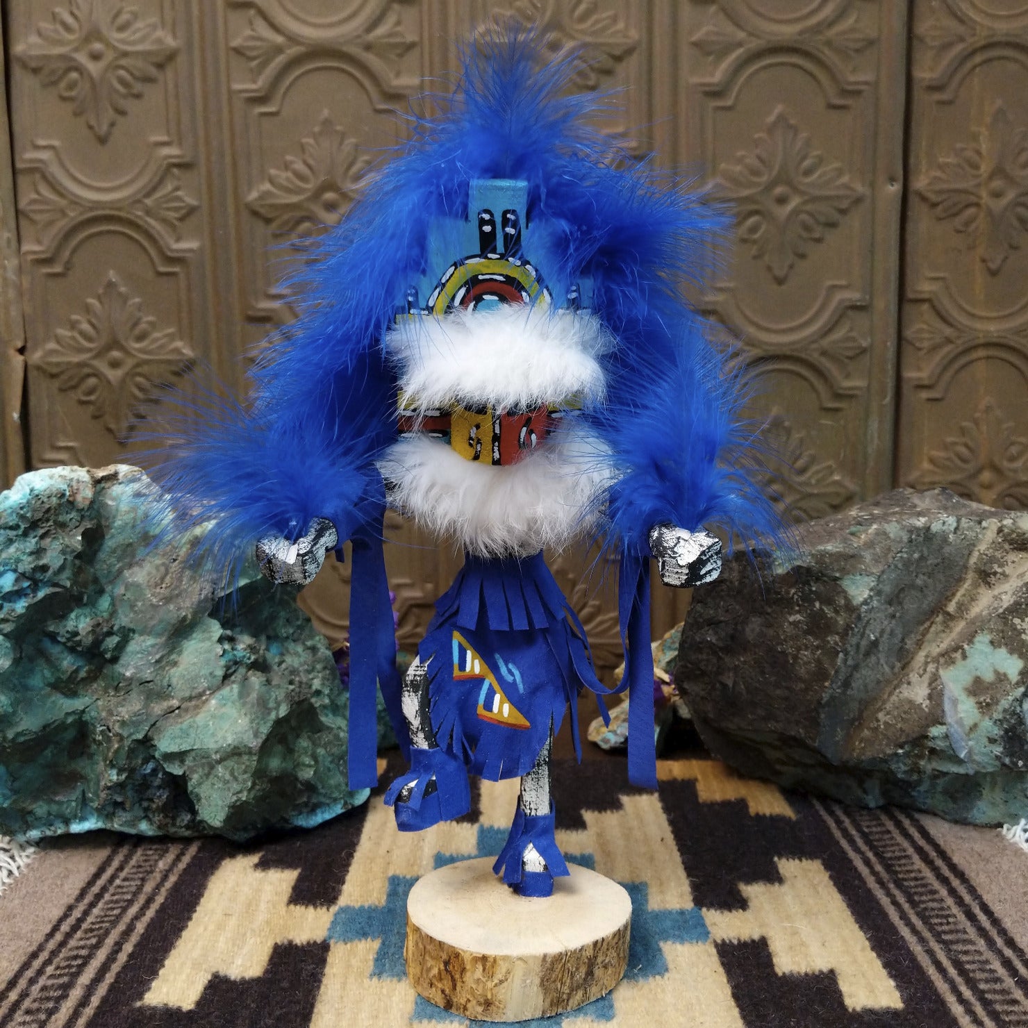 Navajo-made Hemis kachina doll by M. C. with blue feathered headdress, raised leg, and multicolored painted mask.