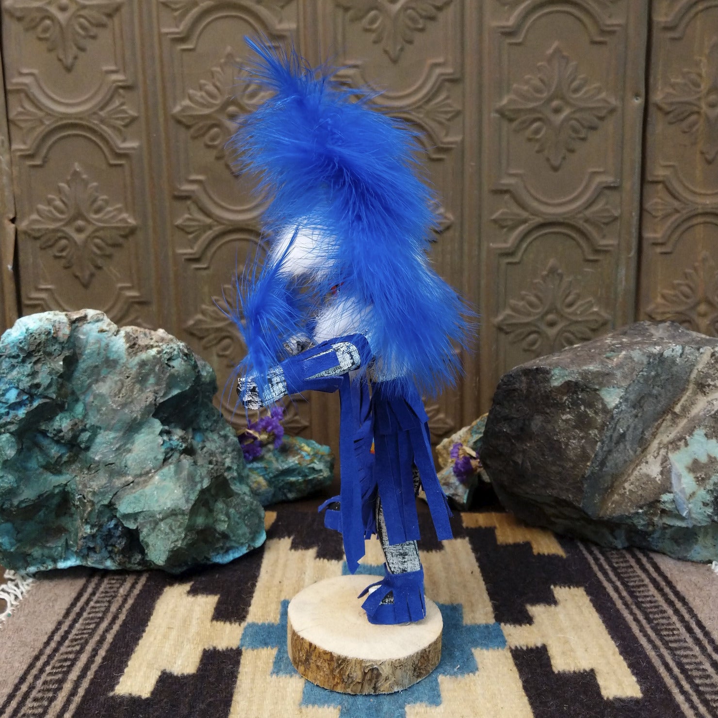 Navajo-made Hemis kachina doll by M. C. with blue feathered headdress, raised leg, and multicolored painted mask.