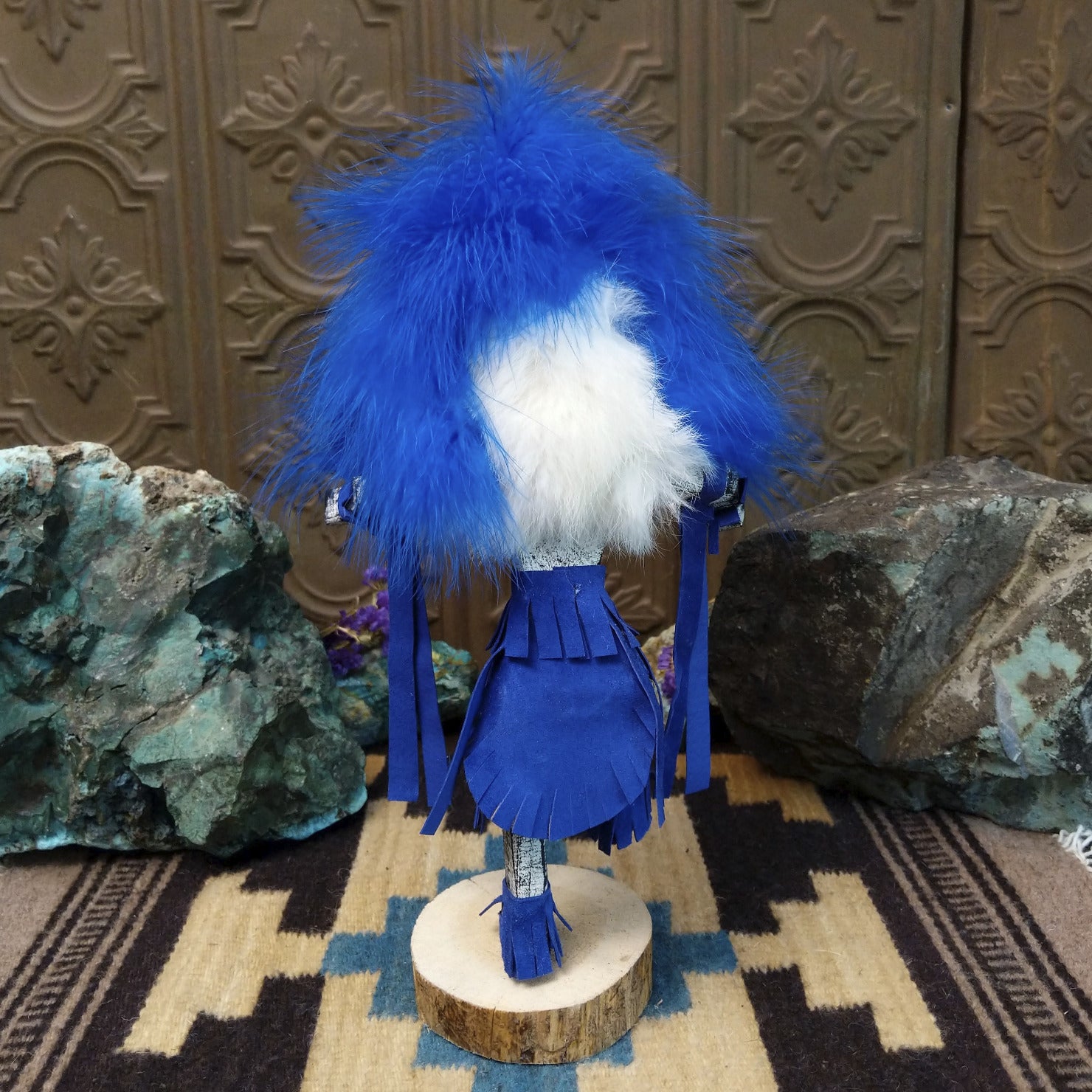 Navajo-made Hemis kachina doll by M. C. with blue feathered headdress, raised leg, and multicolored painted mask.