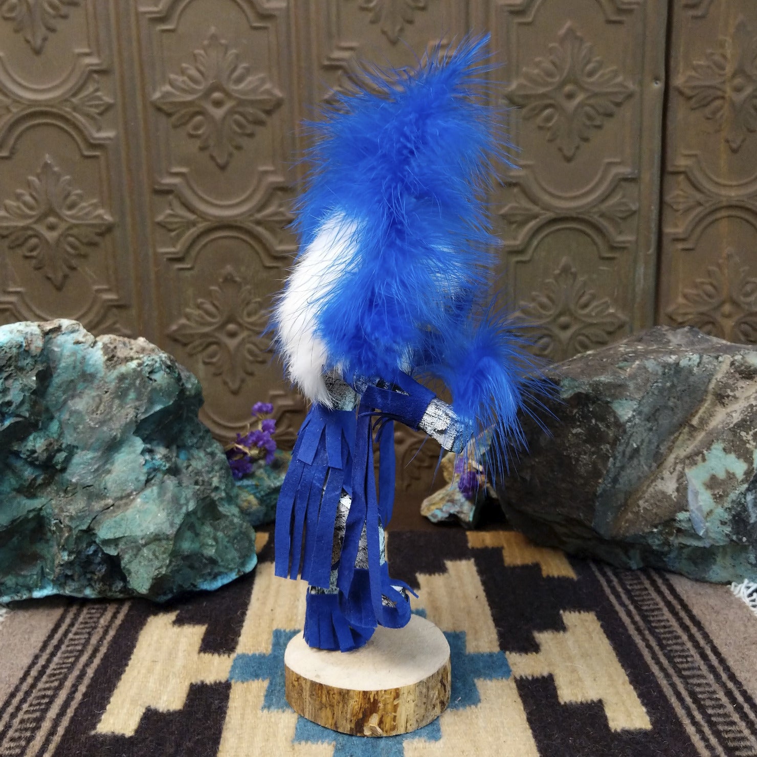 Navajo-made Hemis kachina doll by M. C. with blue feathered headdress, raised leg, and multicolored painted mask.
