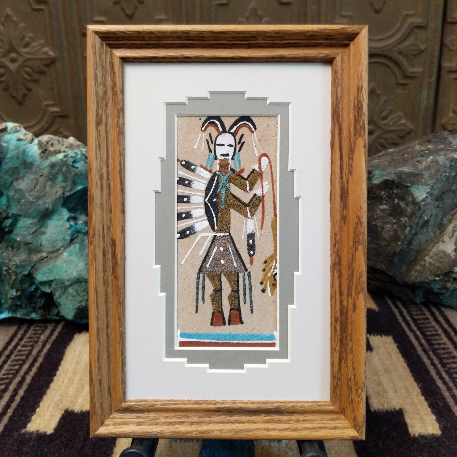 Framed Navajo sand painting of a Hunchback Yei figure with feather details and ceremonial elements.