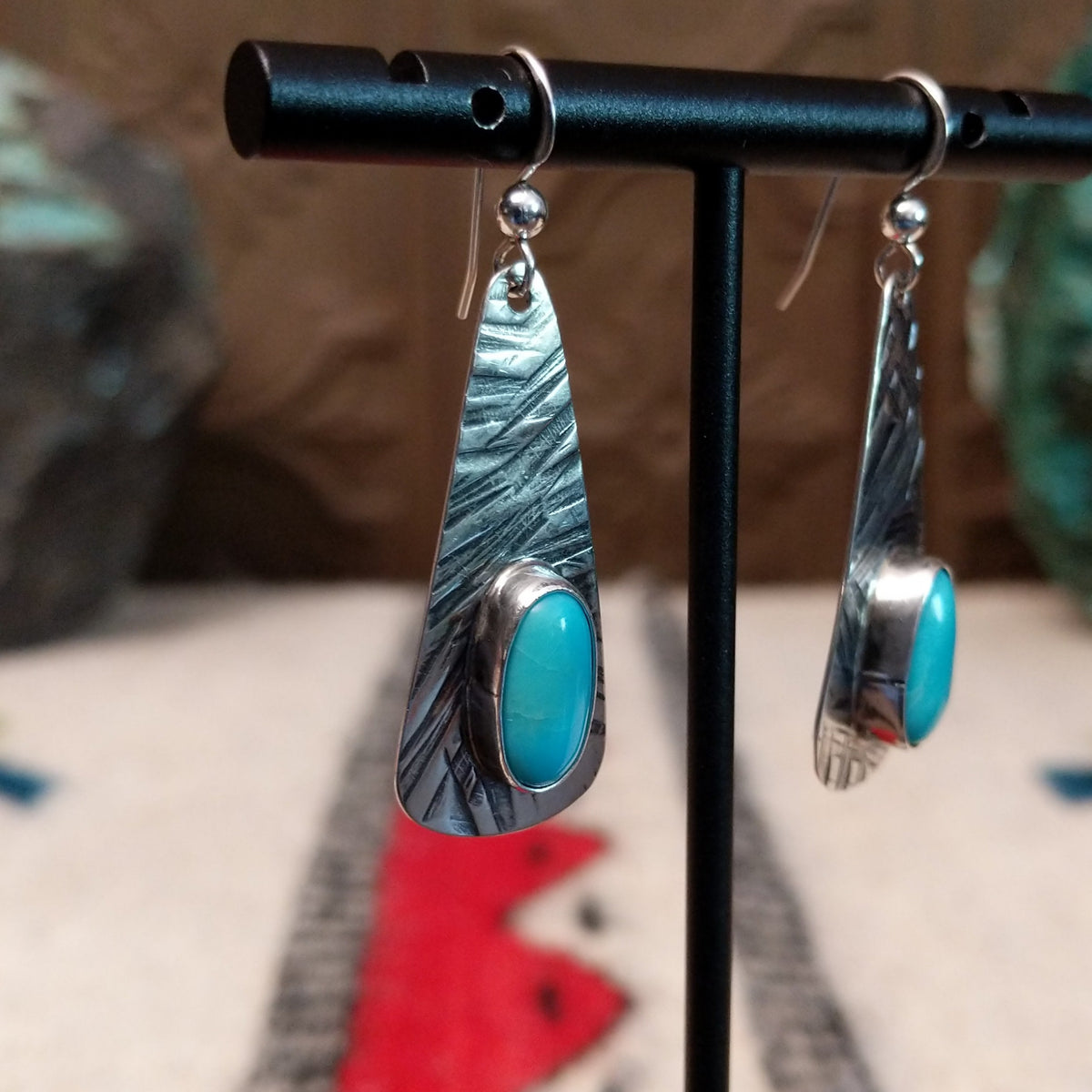 Kingman turquoise earrings by Everett & Mary Teller featuring elongated textured sterling silver drops with oval blue turquoise stones and French wire hooks; side view.